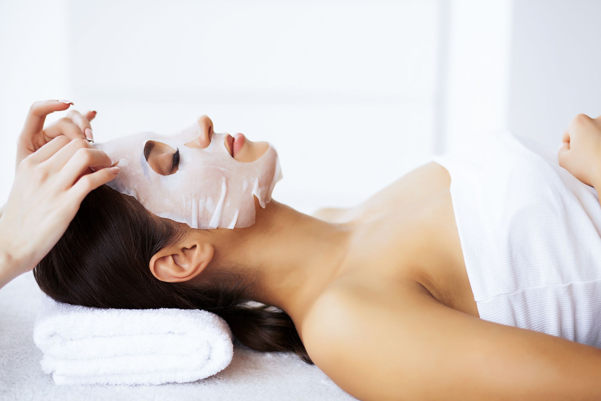 Woman receiving a facial mask in a spa setting, lying on a towel.