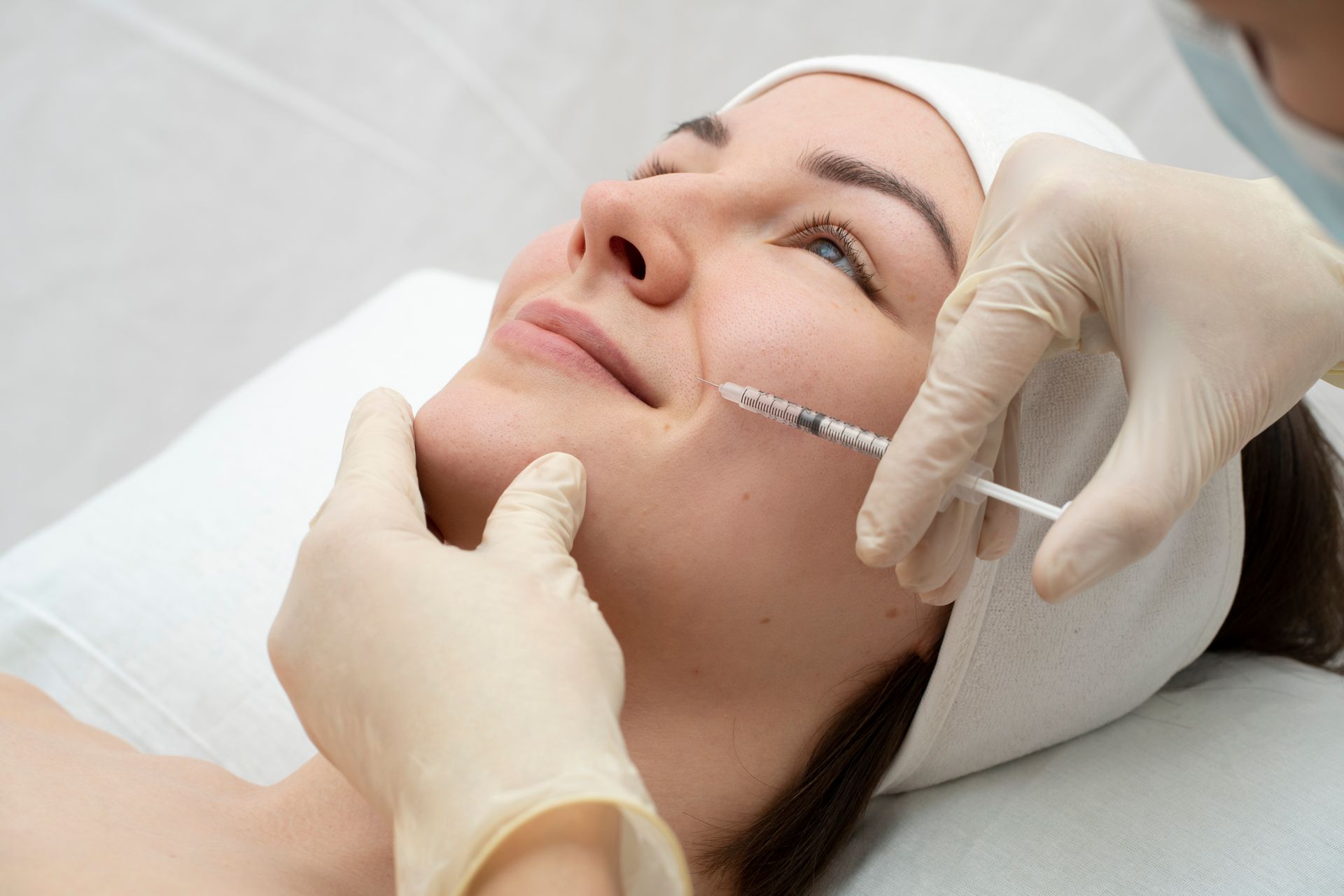 Gloved practitioner injects facial filler into woman lying on a treatment bed