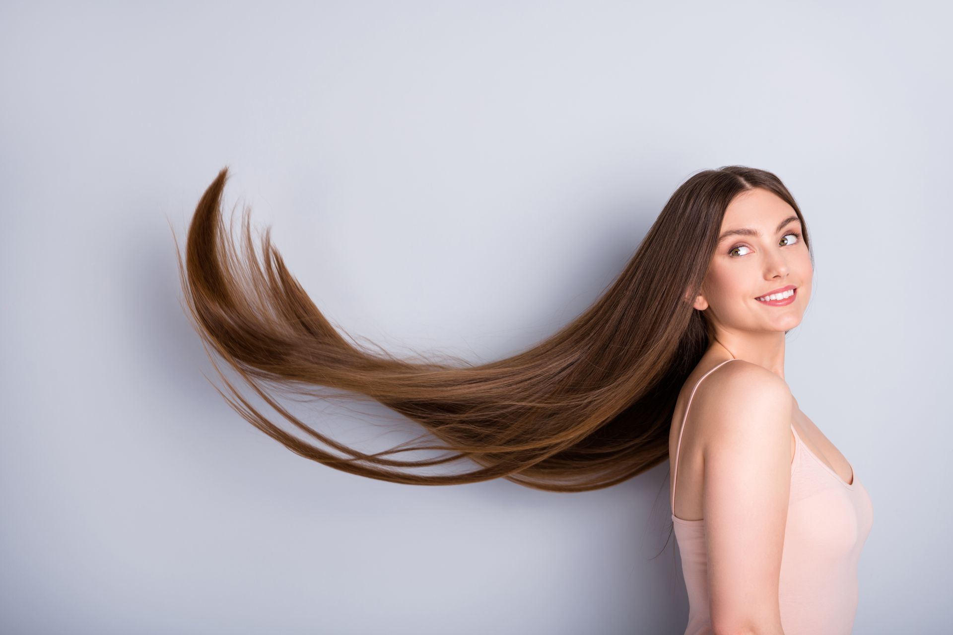 Woman with long brown hair flowing behind her against a light gray background
