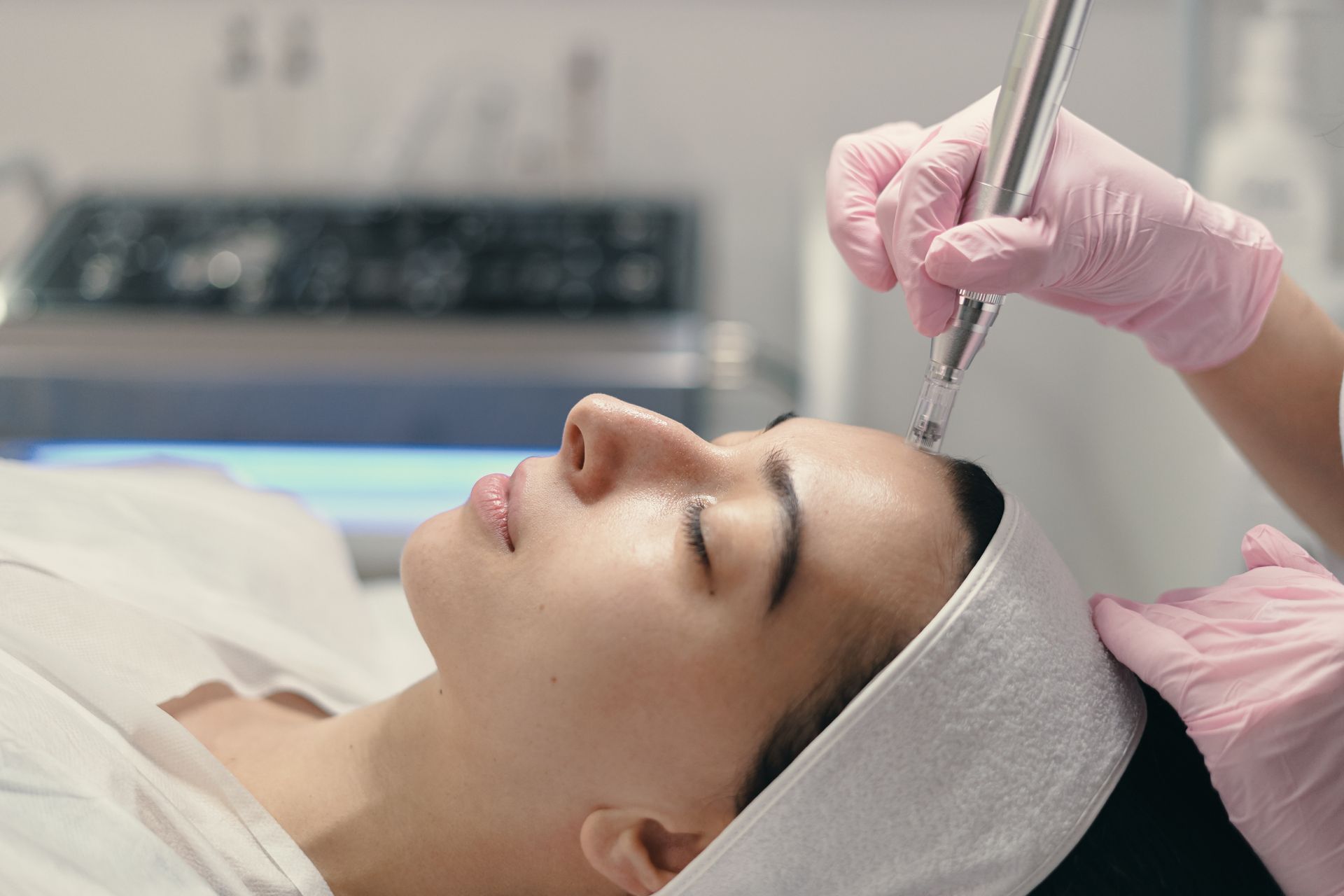 A practitioner in pink gloves uses a facial device on a client’s forehead during a skincare treatment in a clinic.
