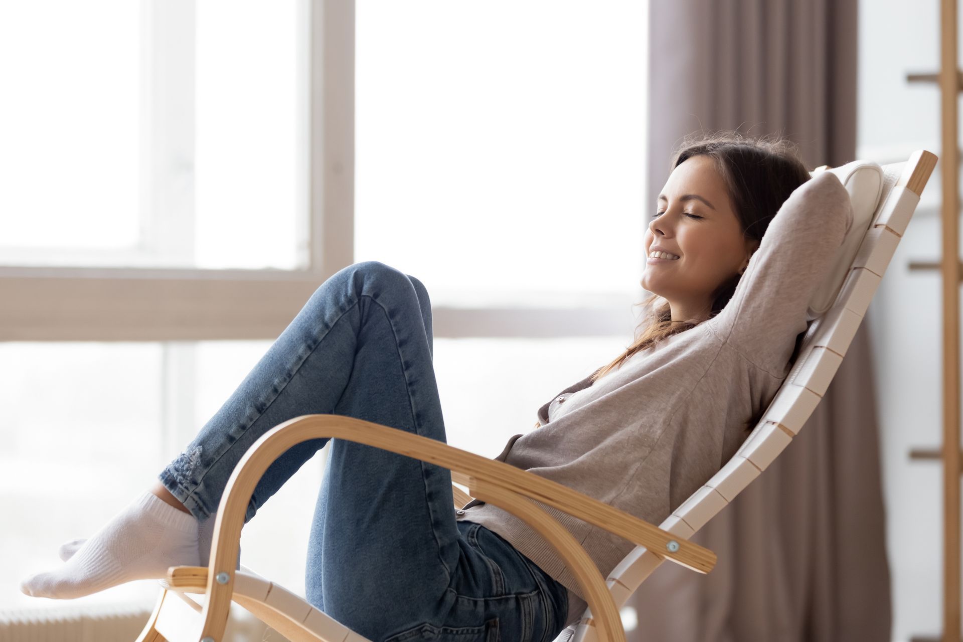 A woman is sitting in a rocking chair in front of a window.