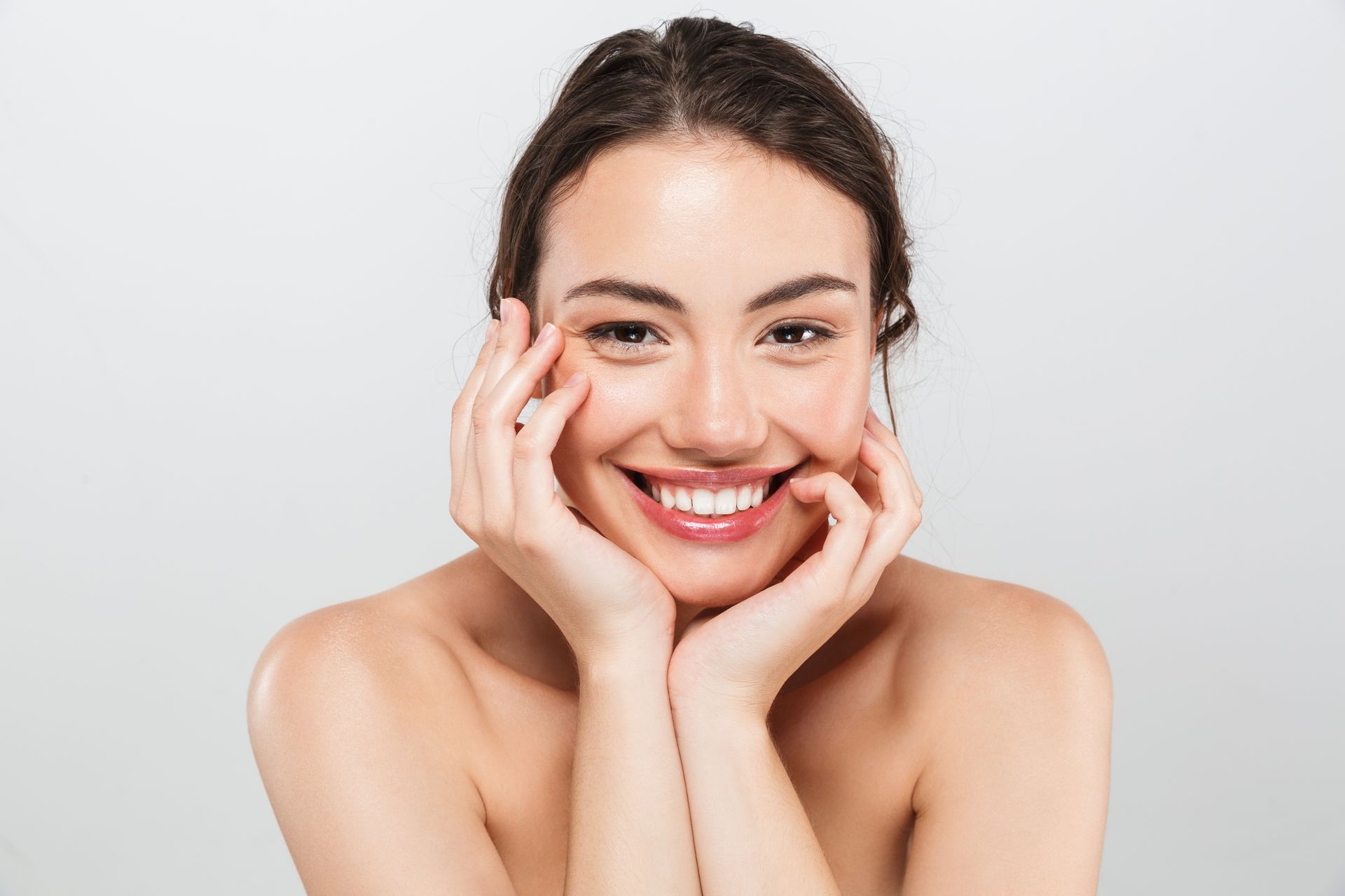 A woman is smiling with her hands on her face.