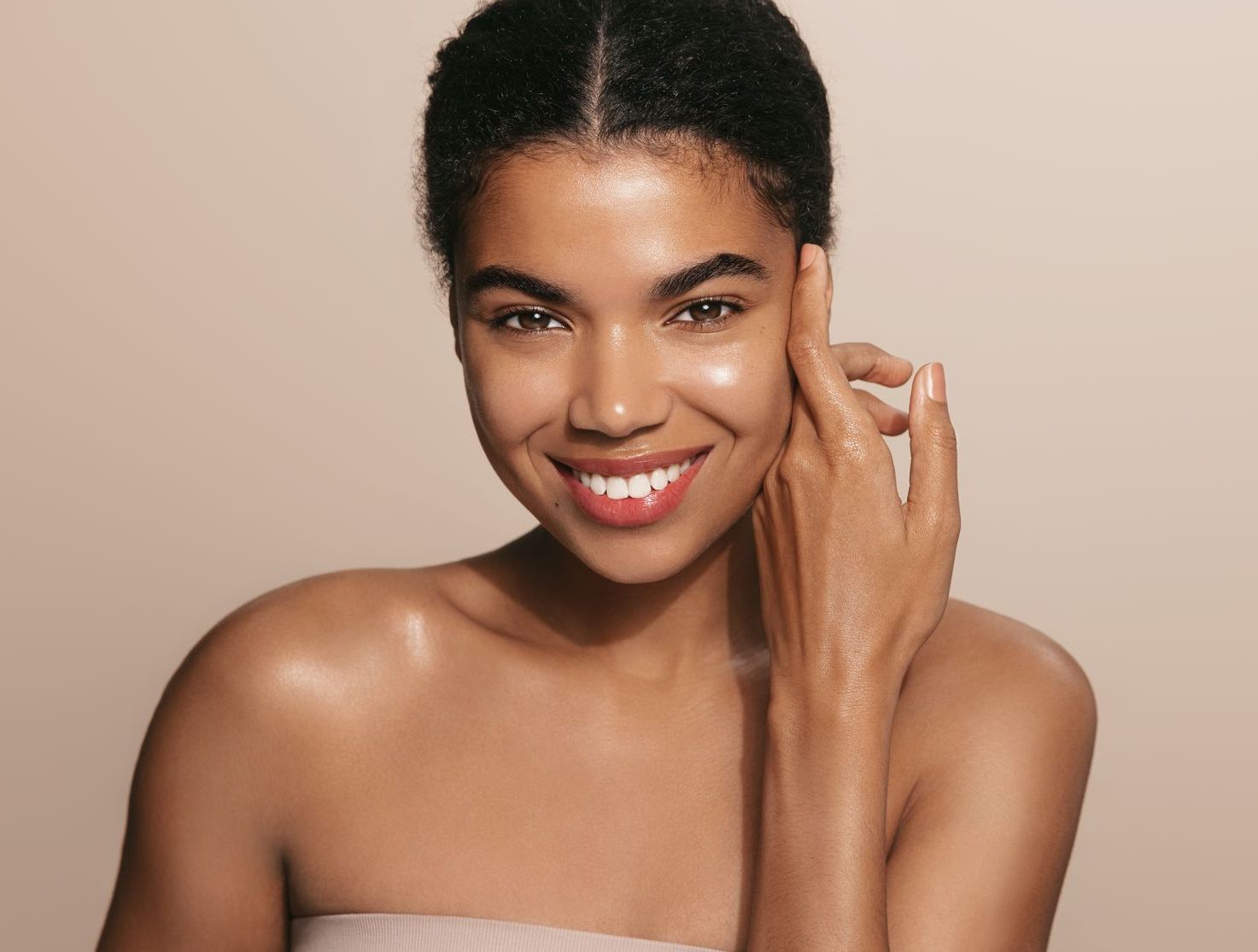 A woman is smiling and touching her face with her hand.
