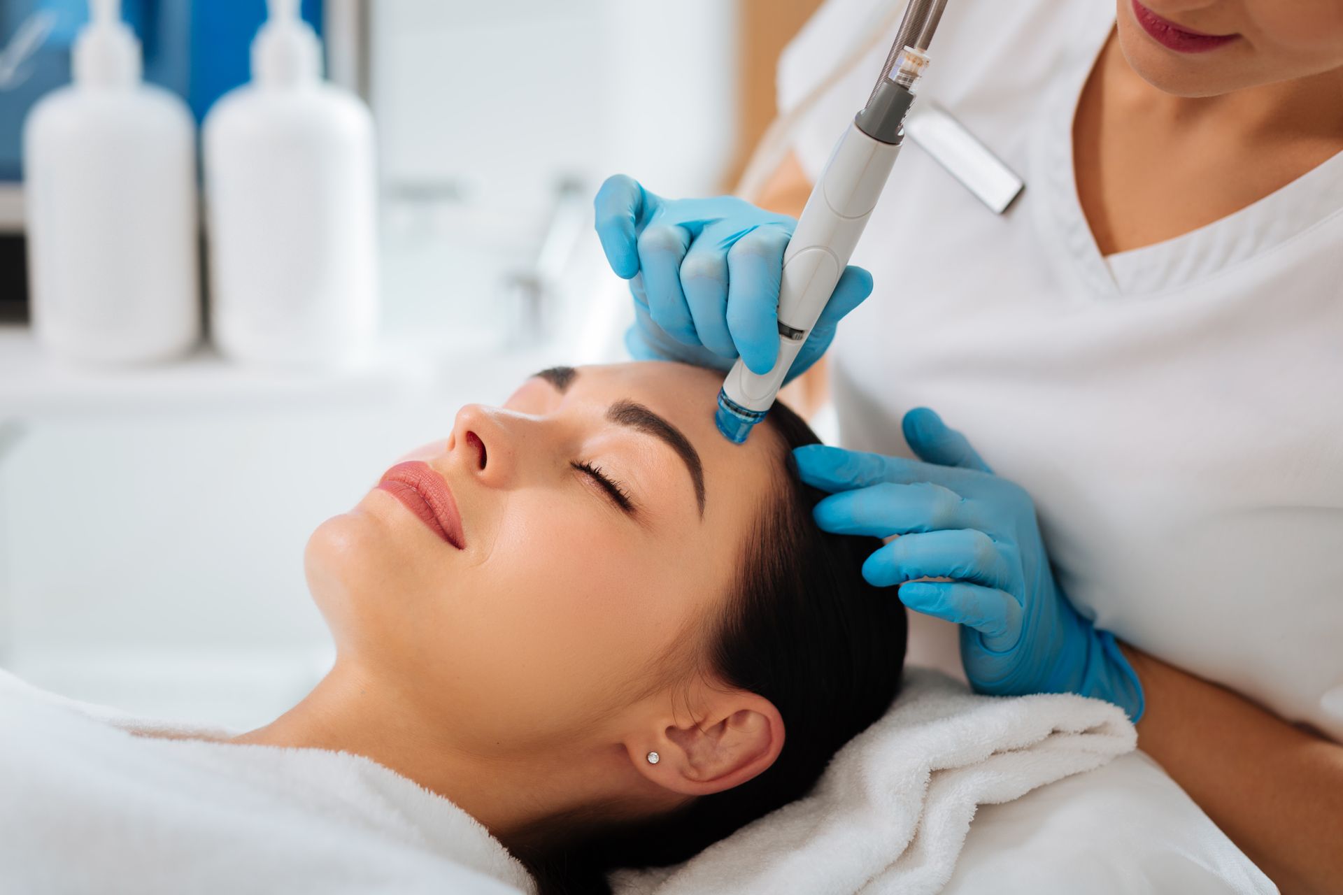 Woman receiving a facial treatment with a handheld device. Skin professional in blue gloves.