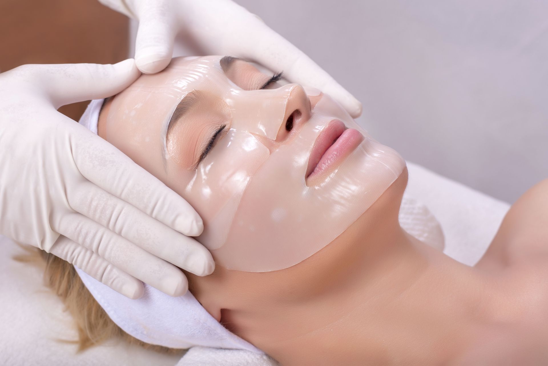 Gloved hands applying a facial treatment mask to a relaxed person lying on a spa bed