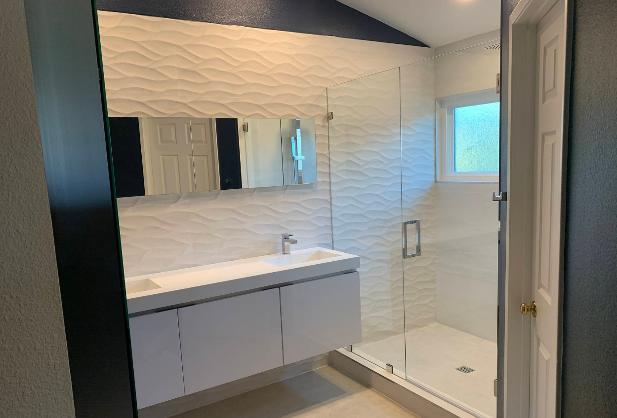 Modern bathroom with white textured tile walls, vanity, and glass shower.