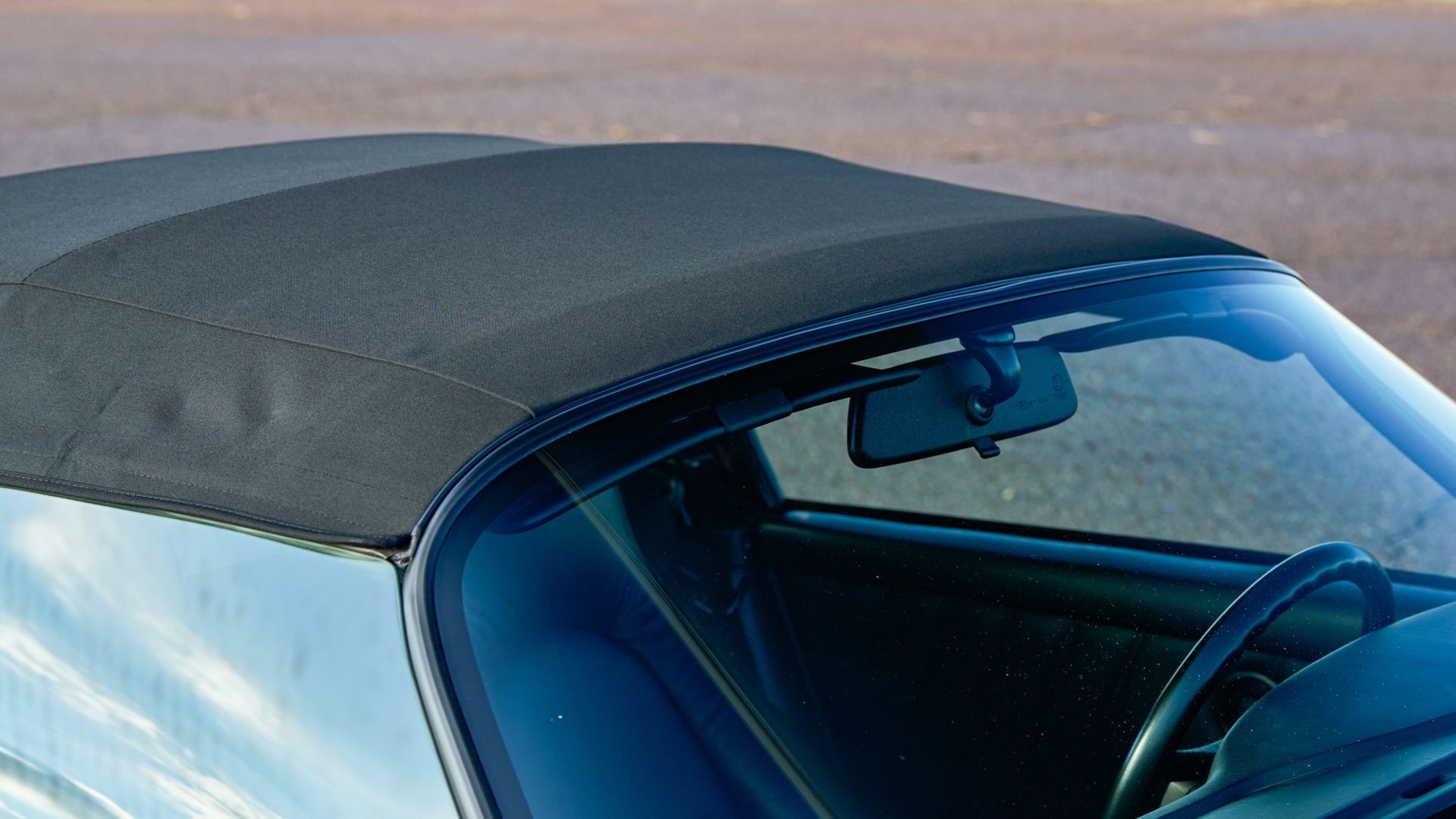 Dark soft-top convertible car roof closeup with windshield and rearview mirror.