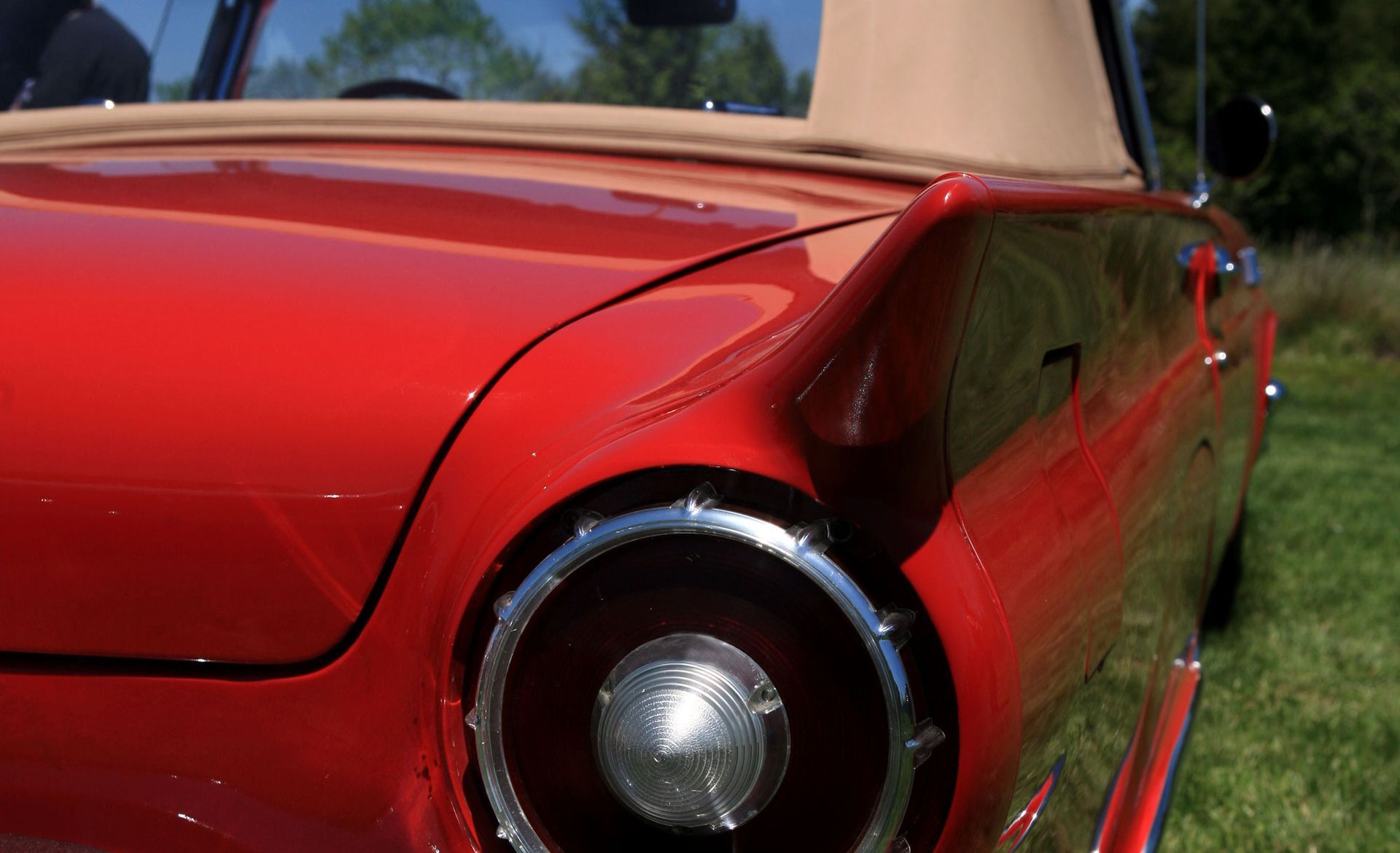 A red convertible parked on lush green grass, with a new convertible top replacement.
