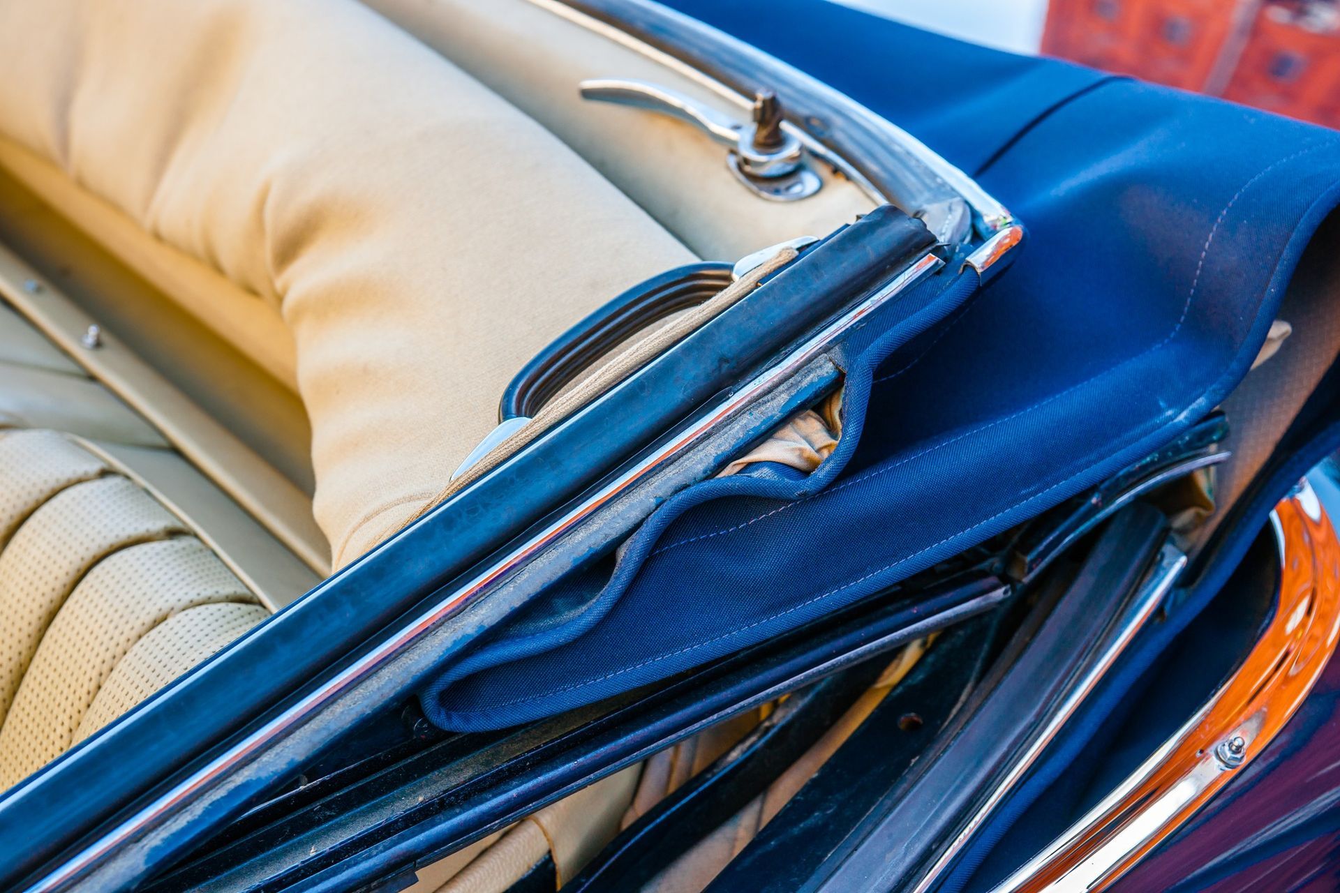 Close-up of folded convertible car roof mechanism with chrome handle and fabric upholstery.