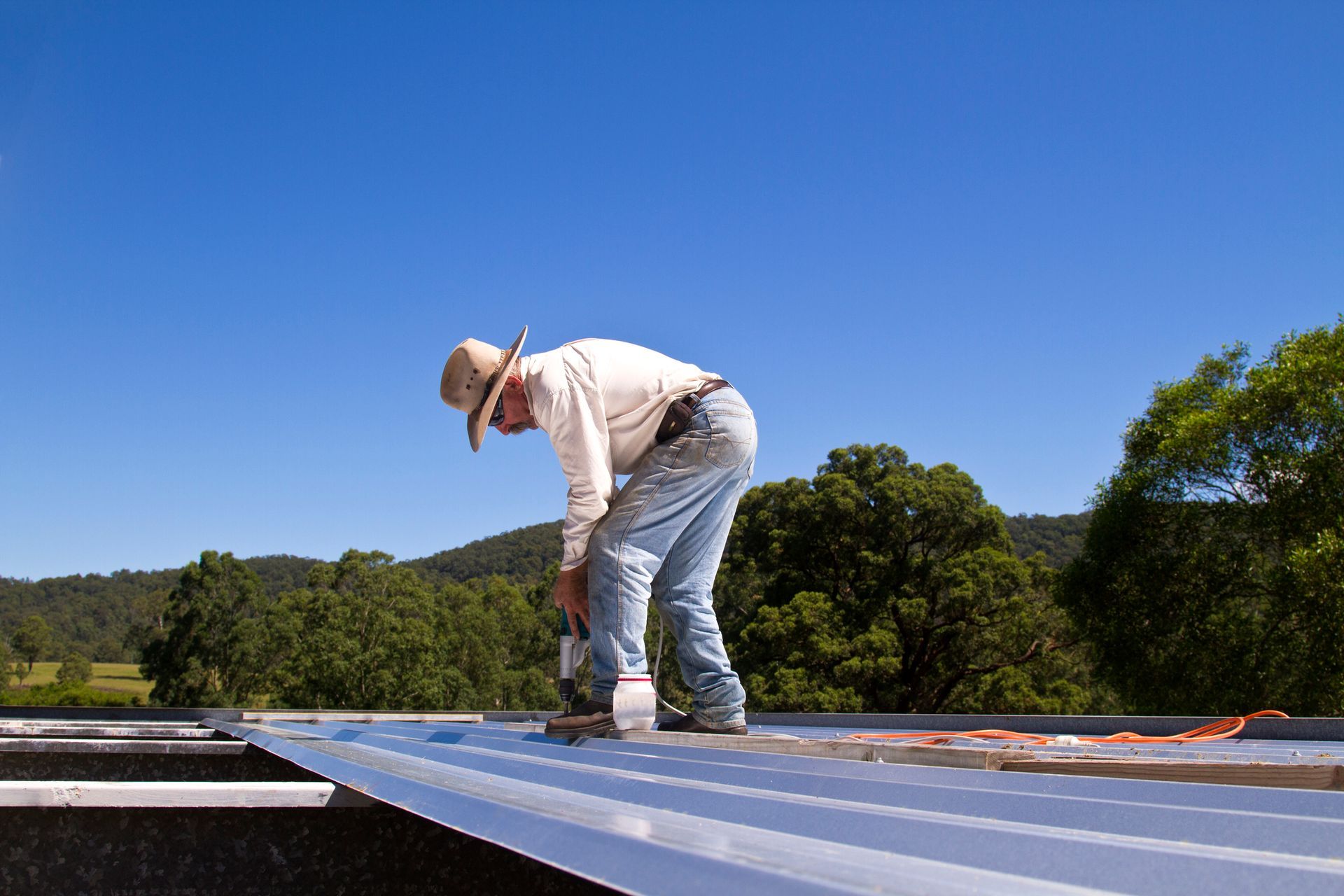 Man On Top Of Roof Drilling In Screws To Secure Metal Sheets – Hornsby Heights, NSW - Donnelly Roof Repairs Pty Ltd