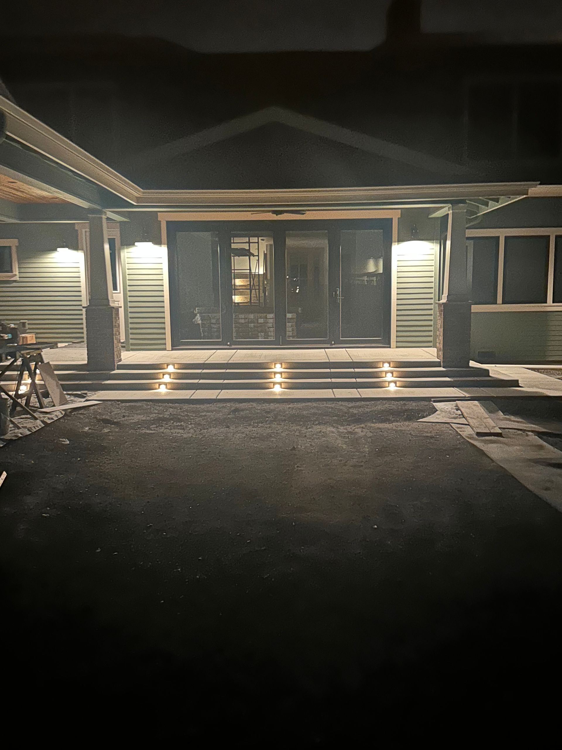 Nighttime view of a lit house entrance with front steps and a dark driveway