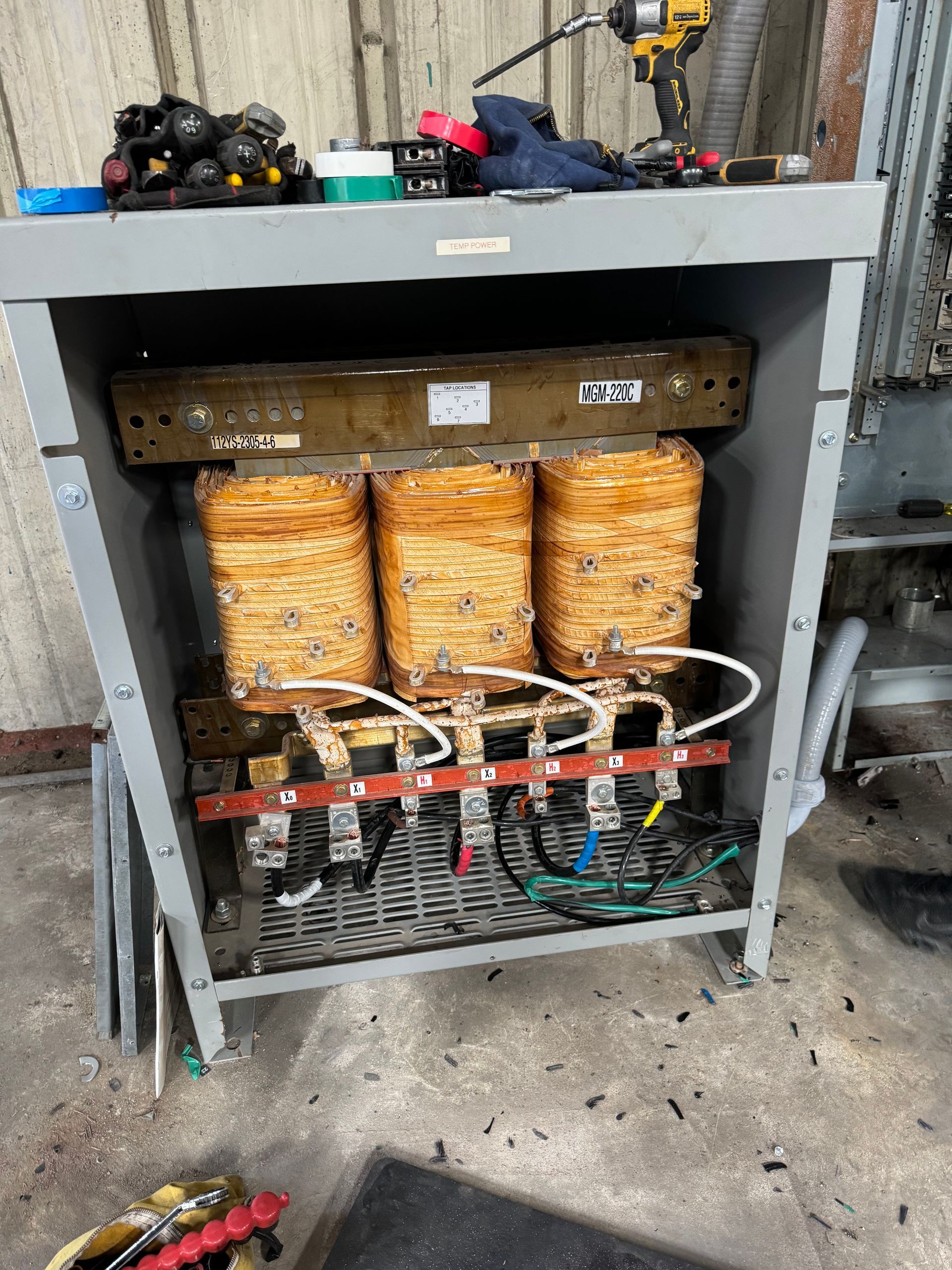 Open electrical cabinet with orange insulated components and wiring on a gray metal frame in a workshop.