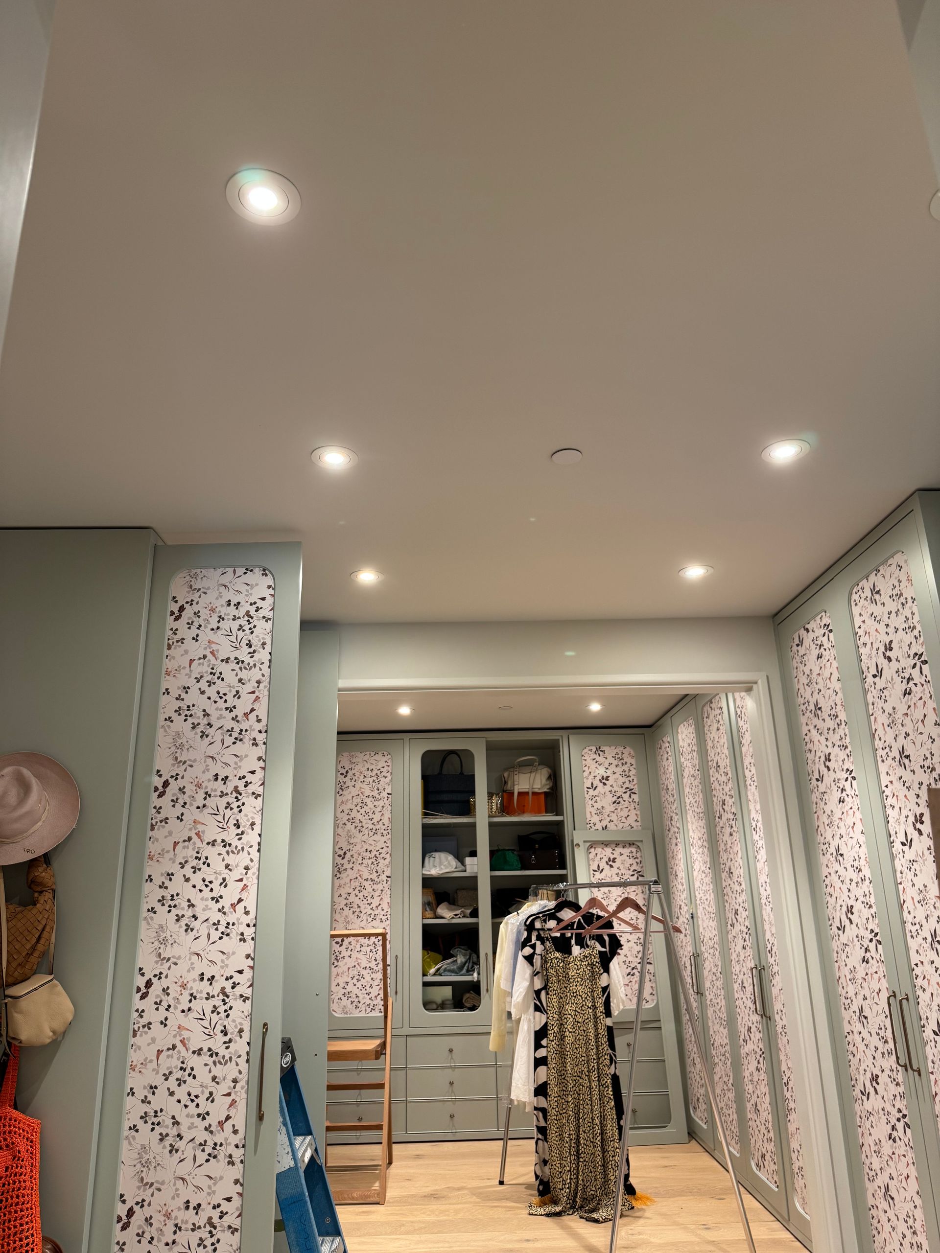 Walk-in closet with floral wallpaper, recessed lights, and patterned clothes on display racks.