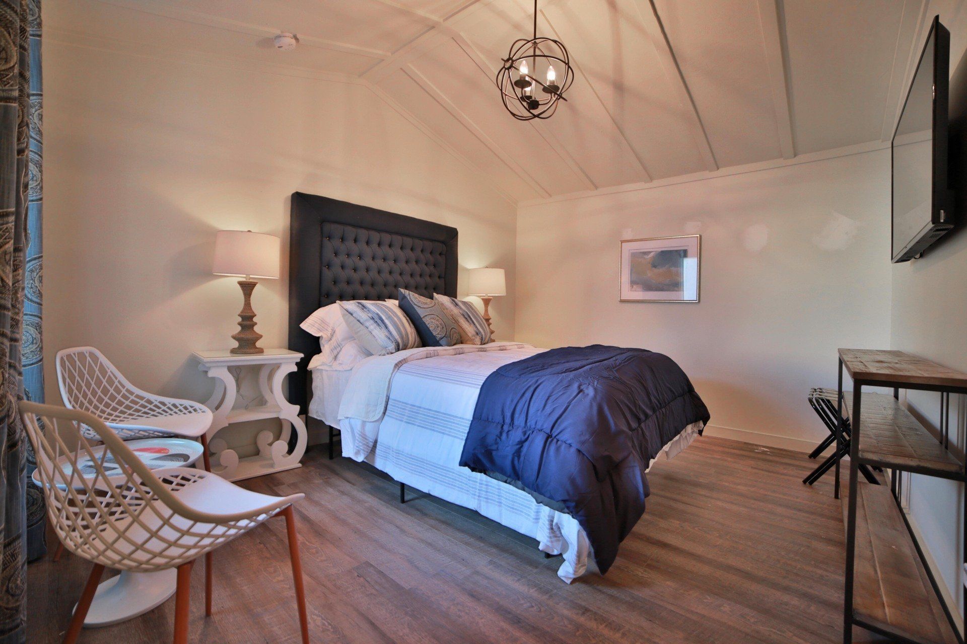 Bedroom with a dark blue bedspread, two white chairs, and a mounted TV.