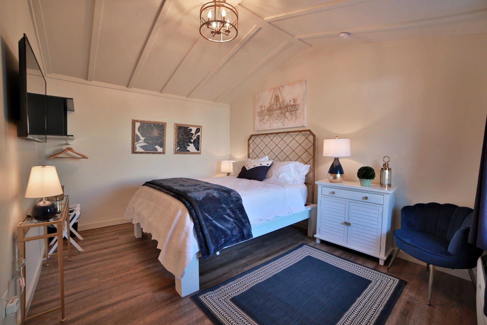 Bedroom with white walls, a bed with blue accents, a white dresser, and a dark blue rug.