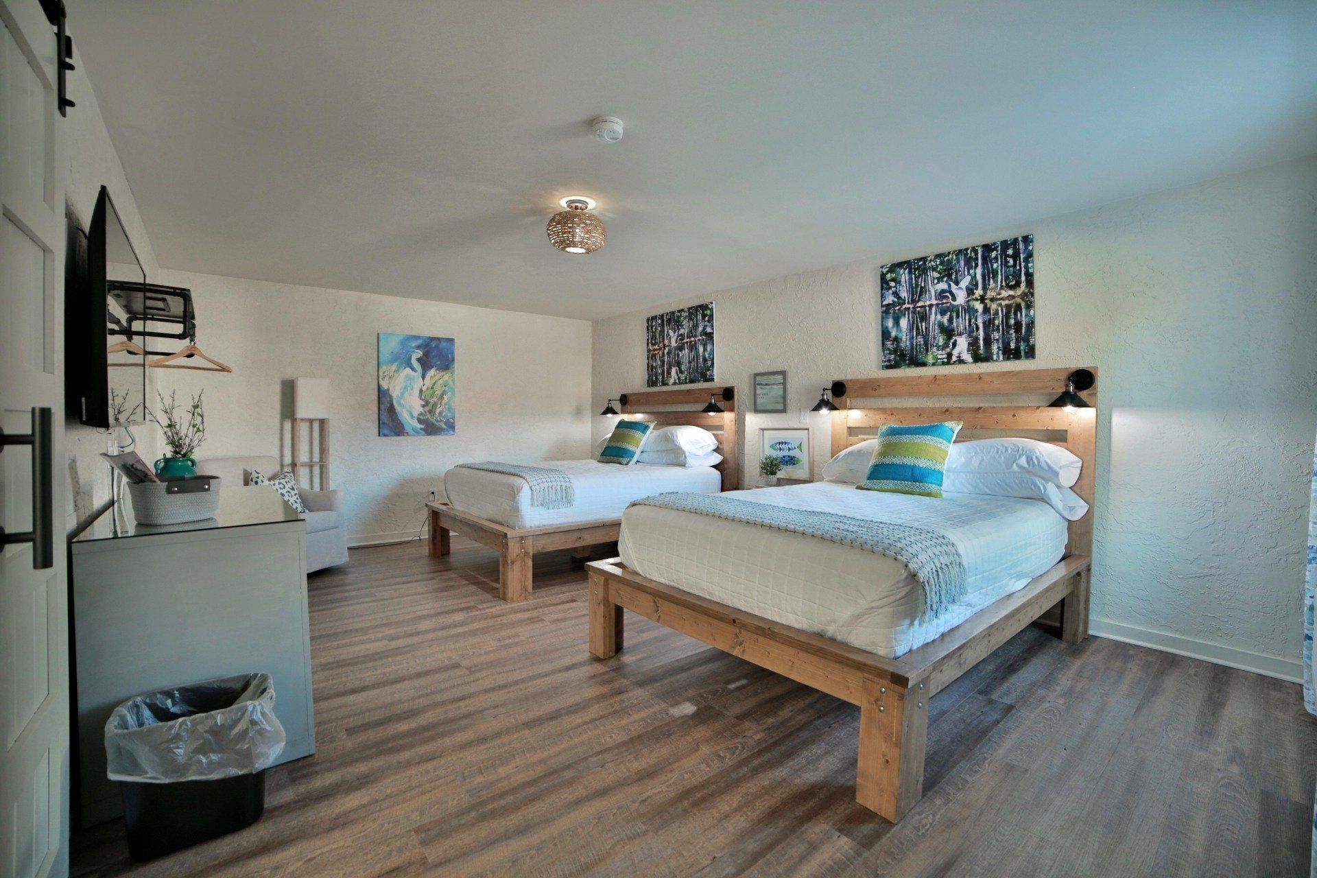 A hotel room with two twin beds, light wood furniture, artwork, and hardwood floors.