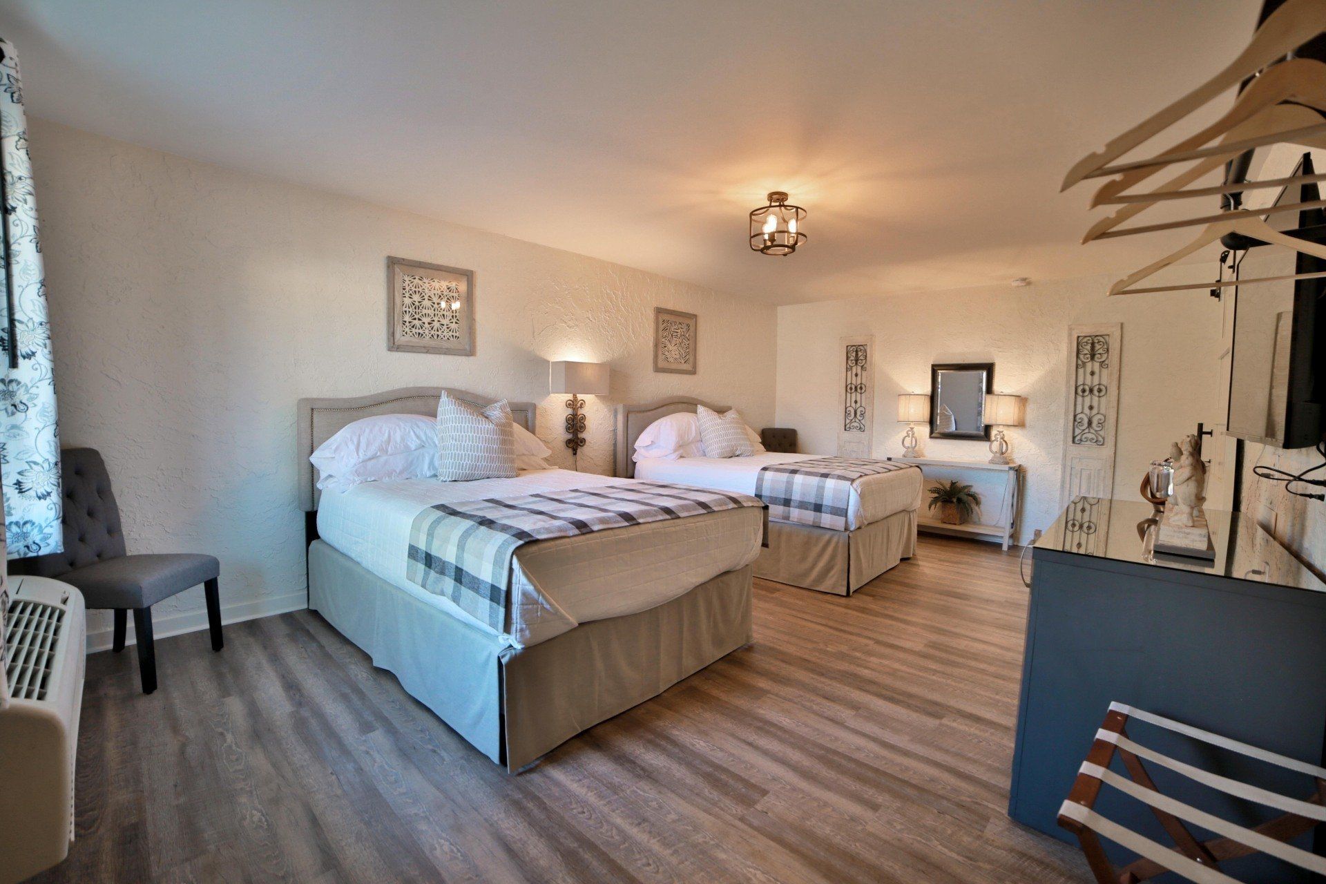 A hotel room with two double beds, gray and white decor, lamps, and wooden floors.