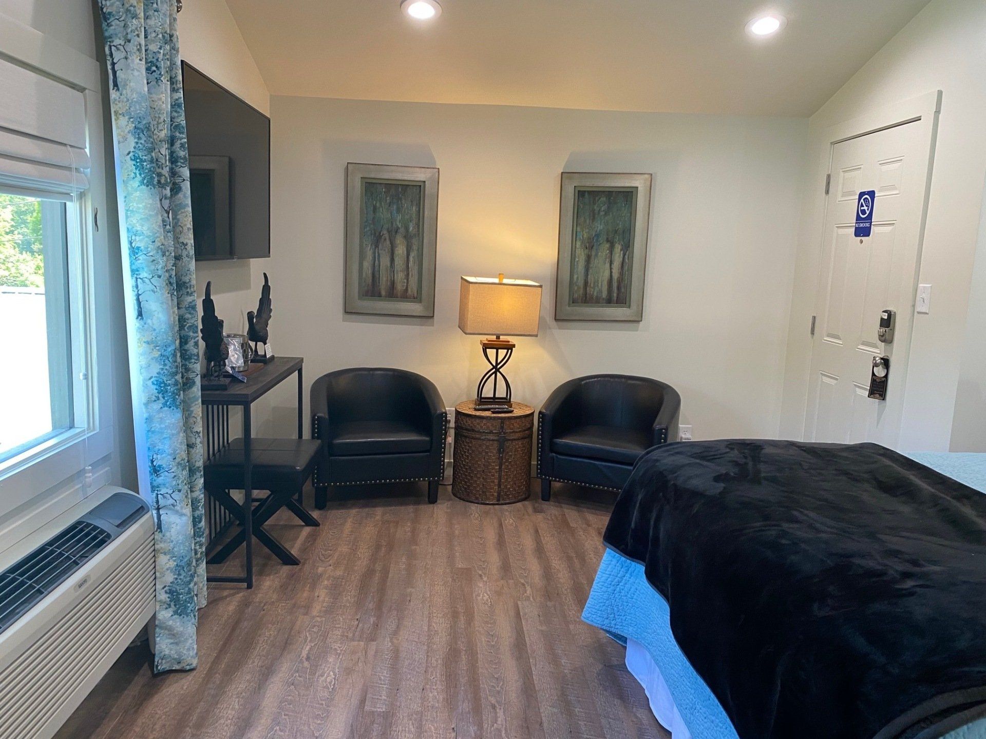 A room with a massage table, two black armchairs, and art. A window with blue patterned curtains is on the left.