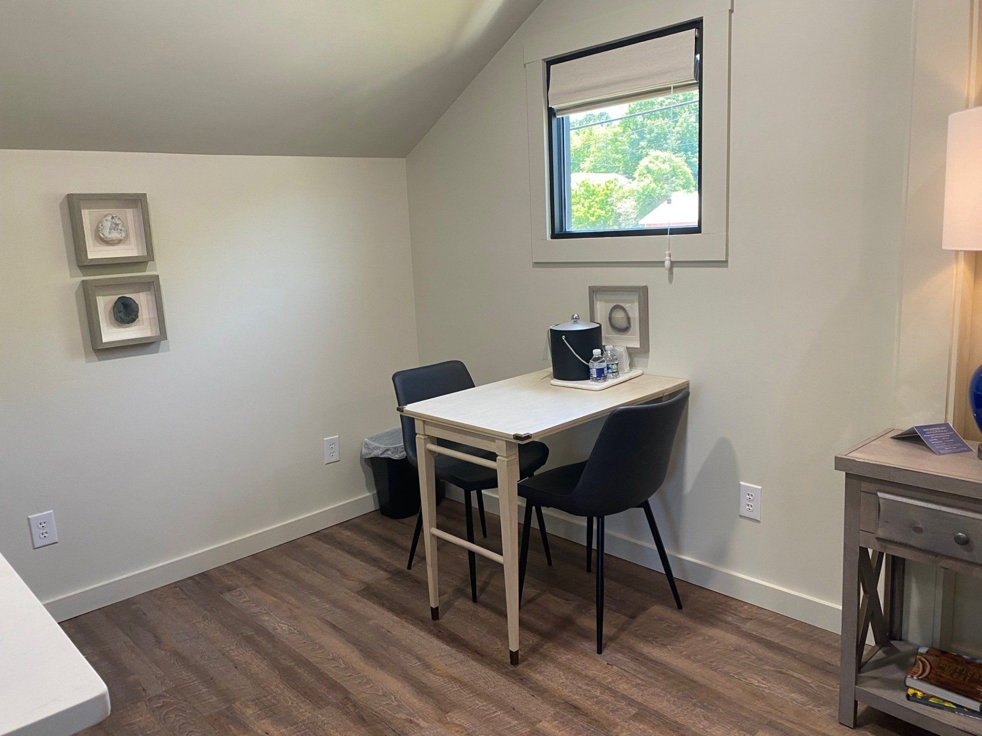 A small room with a table, two chairs, a window, and a bedside table.