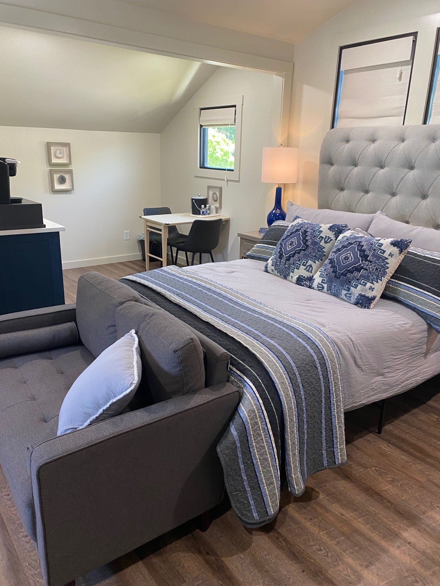 A modern bedroom with a gray tufted headboard, blue and gray bedding, and a gray chaise lounge.