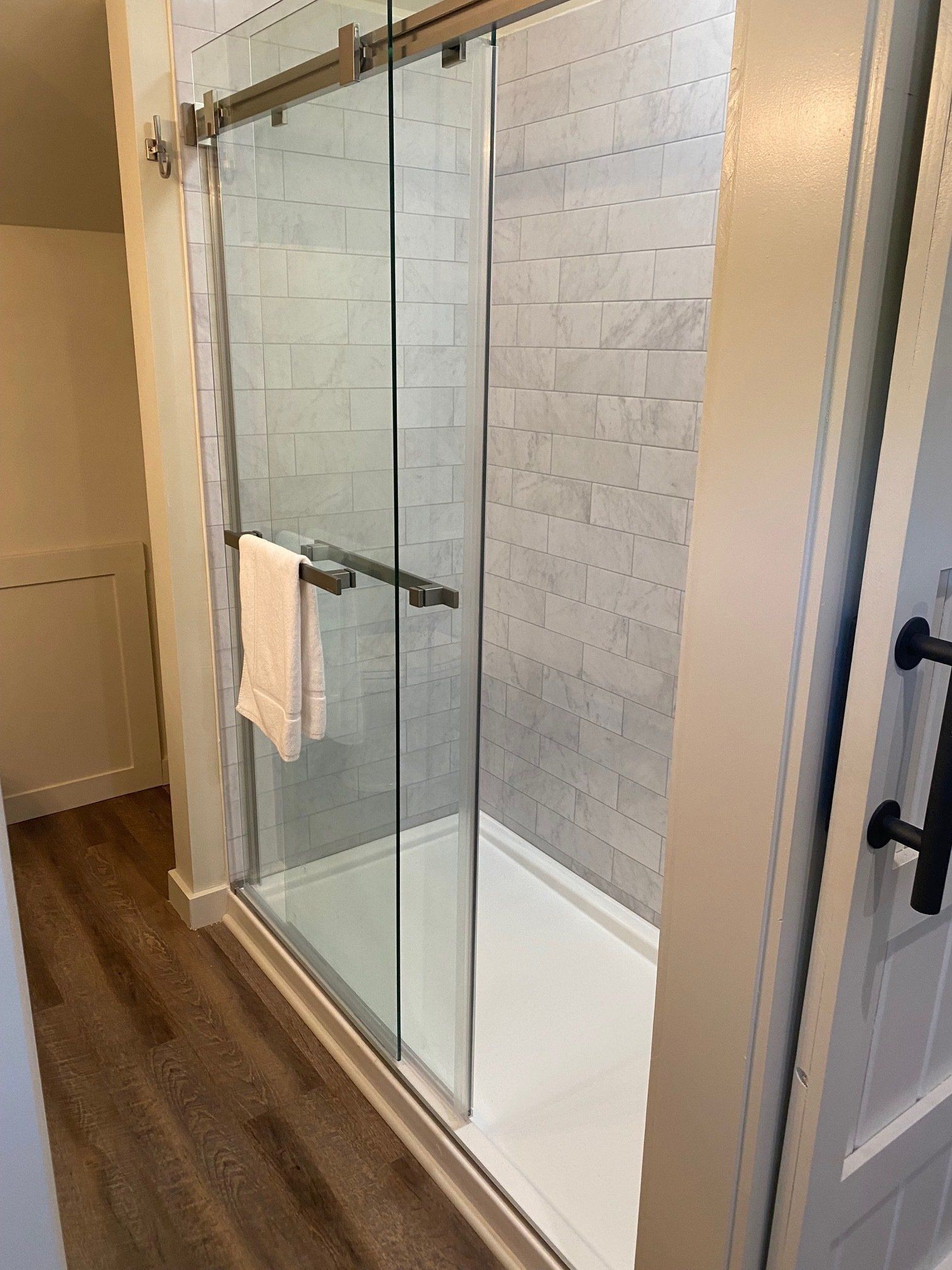 Modern shower with sliding glass doors and white tiled walls. A white towel hangs from a door handle.
