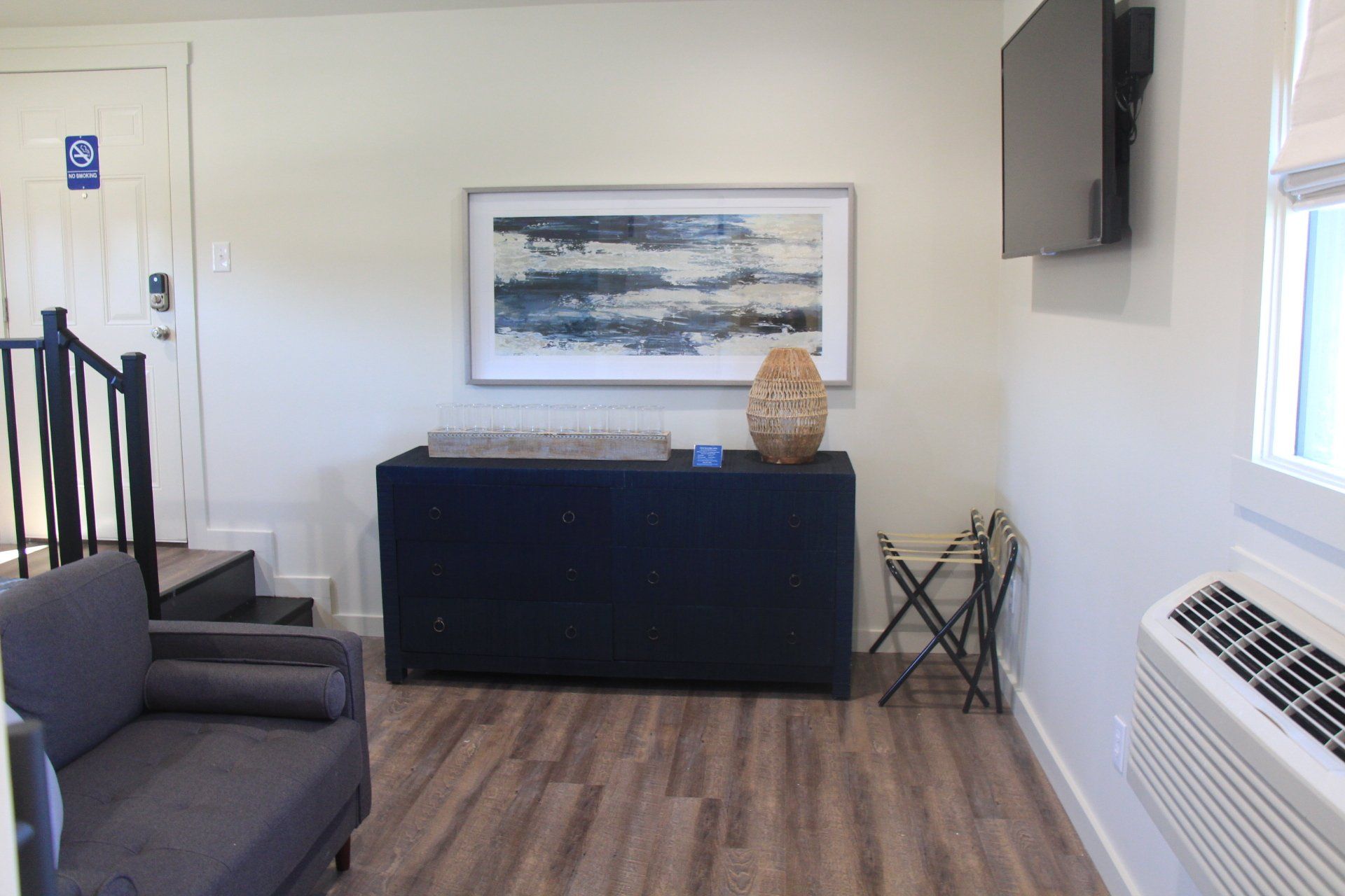 A small room featuring a dark blue cabinet with a framed art piece, a small armchair, and a mounted TV.