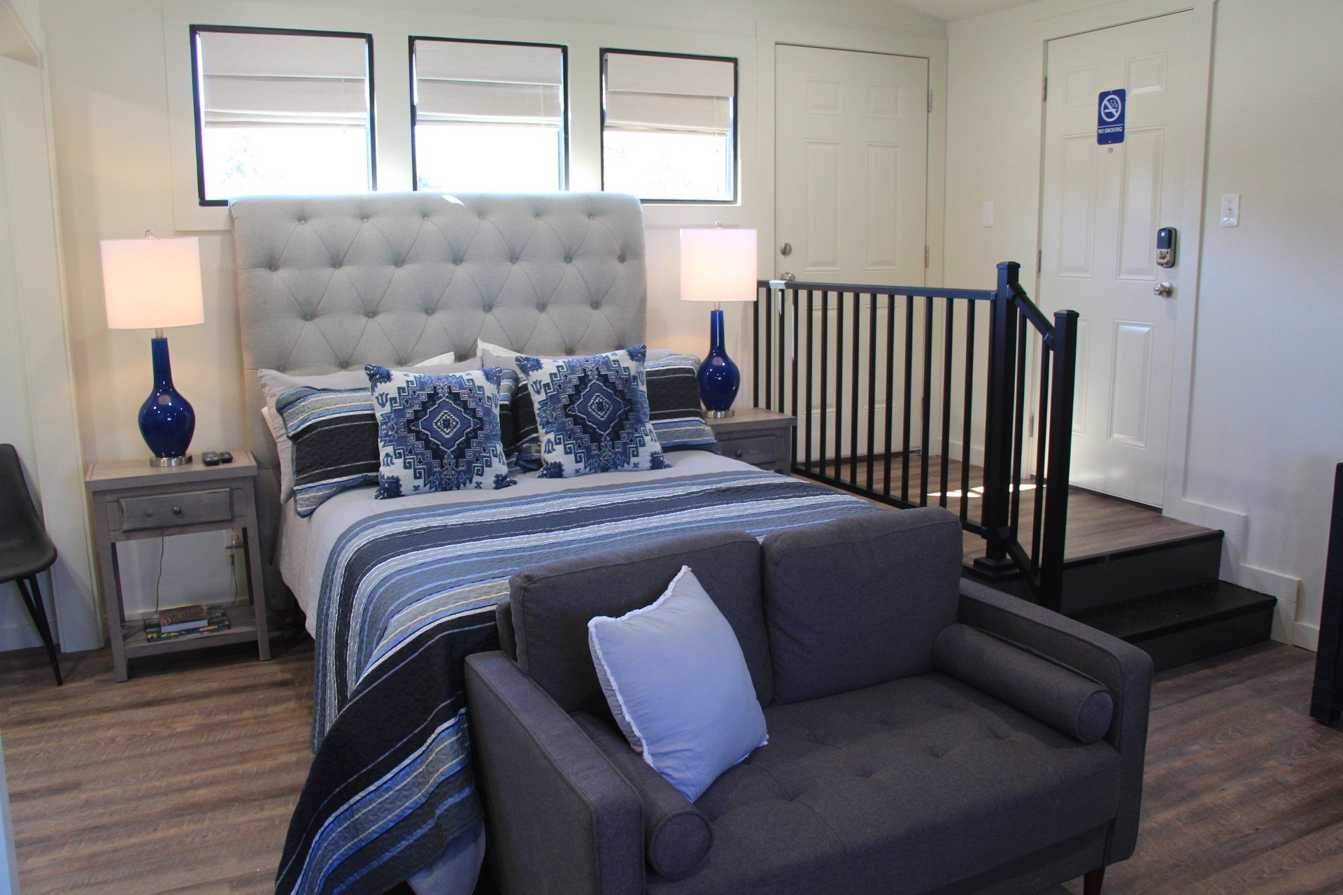 A bedroom with a bed, small couch, and steps leading to a door. Blue and gray color scheme with white walls.