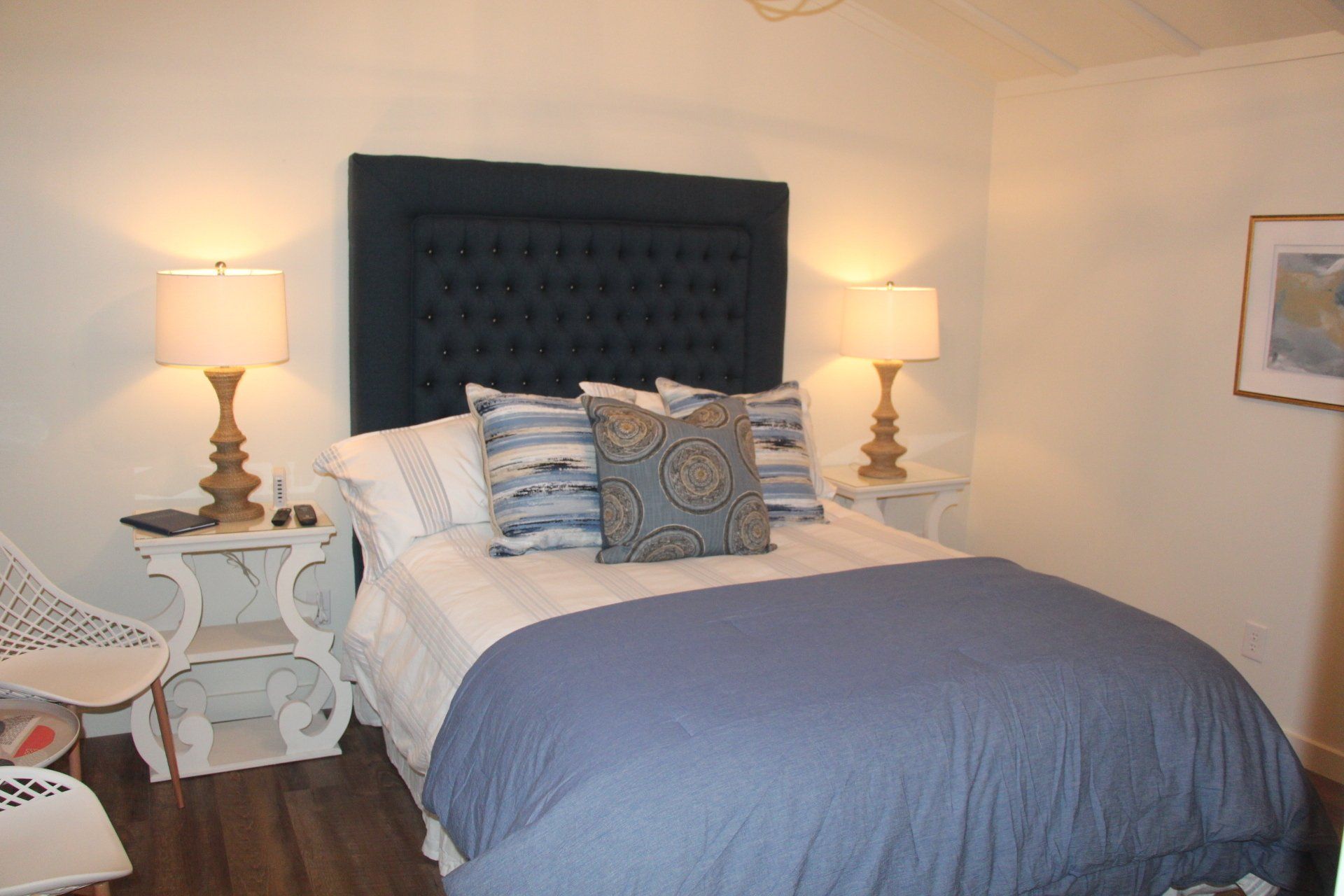 A bedroom featuring a bed with a navy blue headboard and bedding, flanked by two lamps on bedside tables.