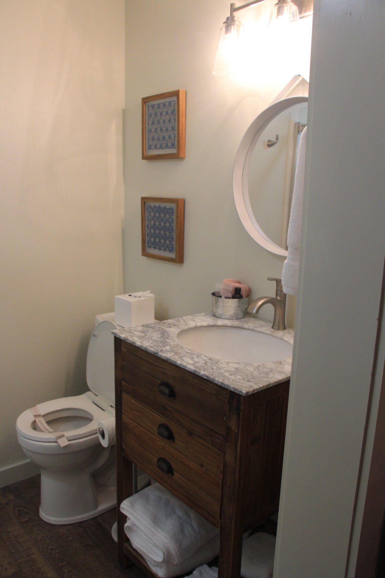 A small bathroom with a toilet, sink, and mirror. Two framed decorative squares hang on the light green wall.