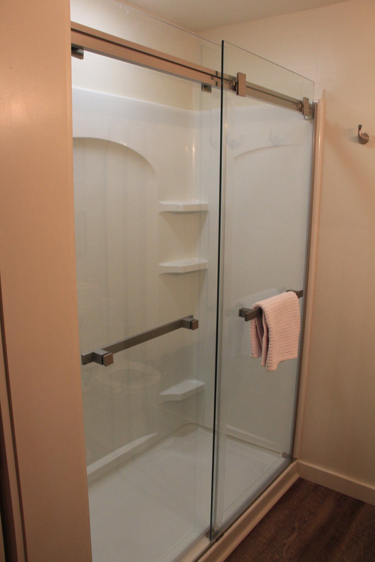 A shower stall with sliding glass doors, grab bars, and built-in shelves. A towel hangs on the door.
