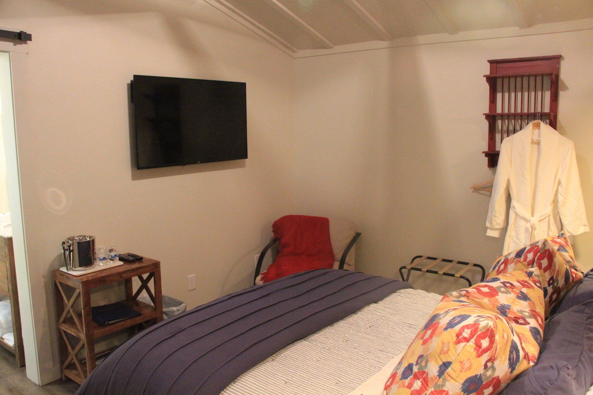 Bedroom interior with a bed, television, and small side table. A robe hangs on a wall-mounted rack.