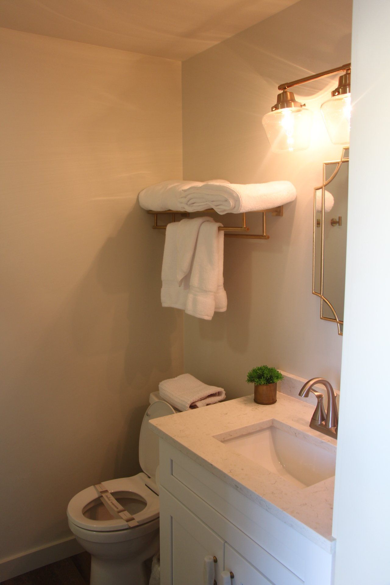 A small bathroom featuring a toilet, vanity with sink, and towels hanging on a rack; a light fixture is above the mirror.