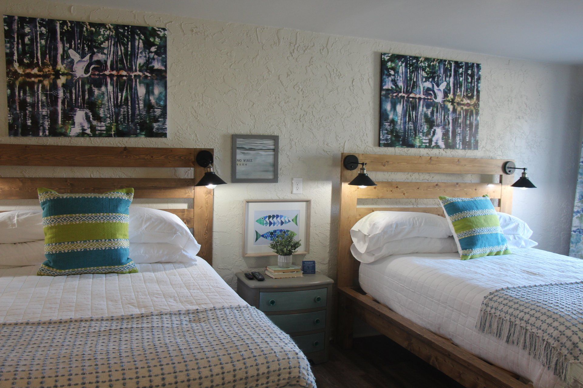 Two beds with white bedding and colorful pillows under art in a room with textured walls.