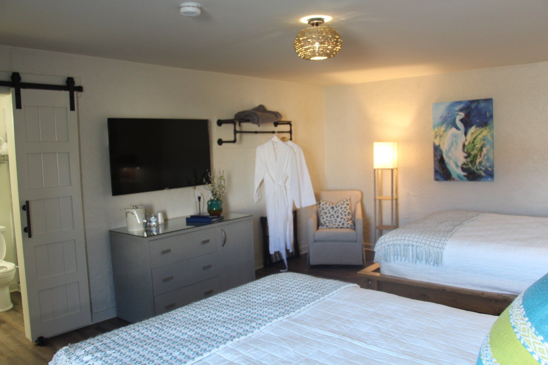 A hotel room with two beds, a dresser, TV, and bathroom door.  A white robe hangs on a wall rack.