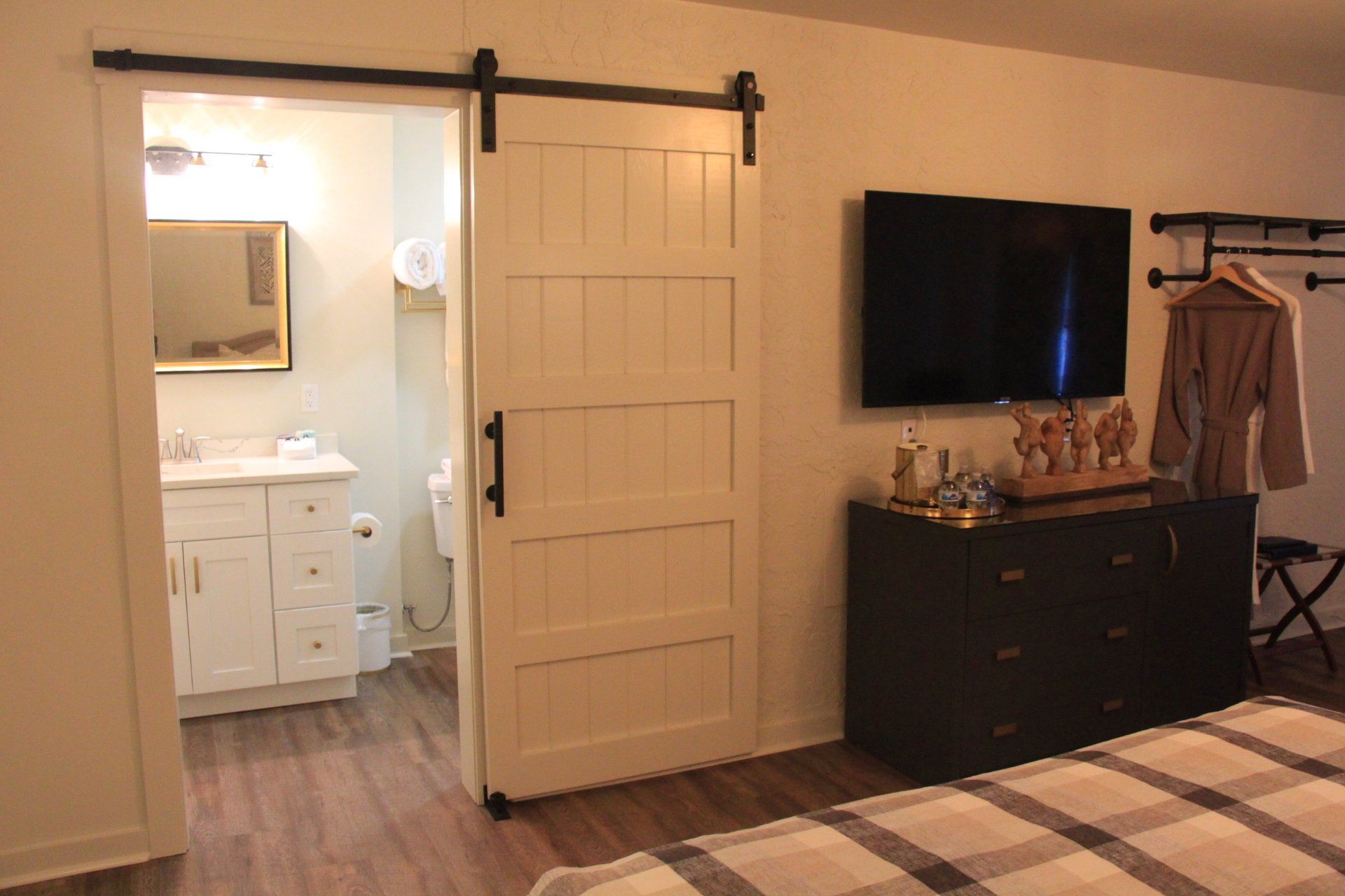 White sliding barn door partially open to a bathroom. A TV hangs on the wall above a dark dresser in the bedroom.