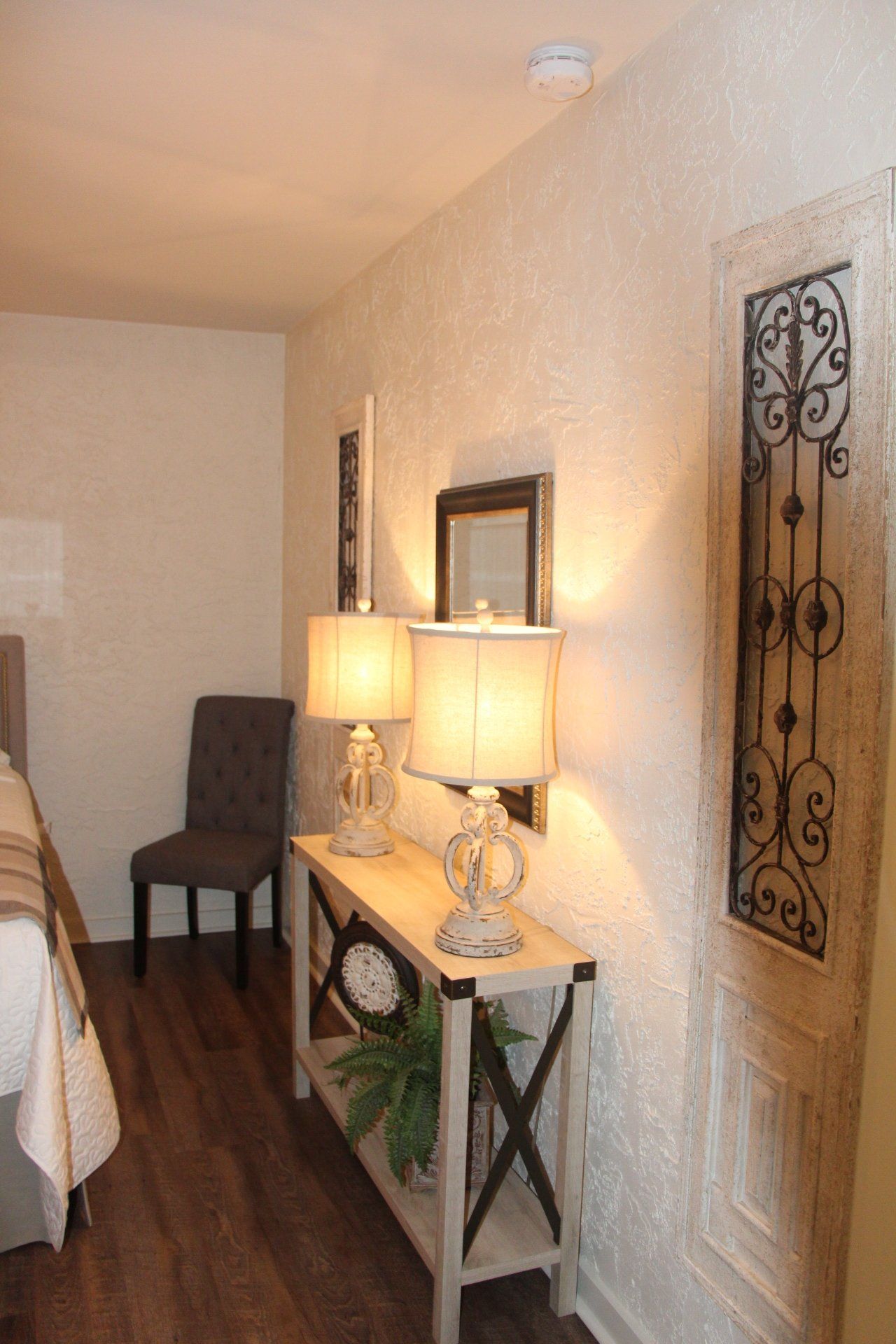 A hallway featuring a wooden console table with two lamps, a framed mirror, and a decorative door on the right. 