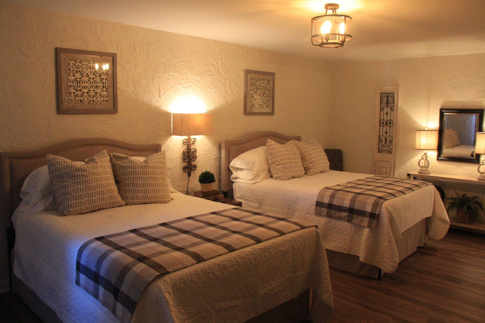 A hotel room with two queen beds, lamps, and decorative art on the walls. The room is warmly lit.