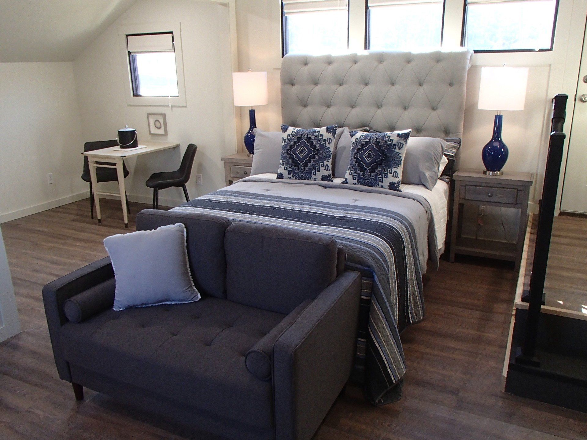 Bedroom with a large tufted headboard, small sofa, desk, and wooden floors; blue and gray color scheme.