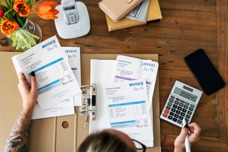 A woman is sitting at a table with a calculator and papers.