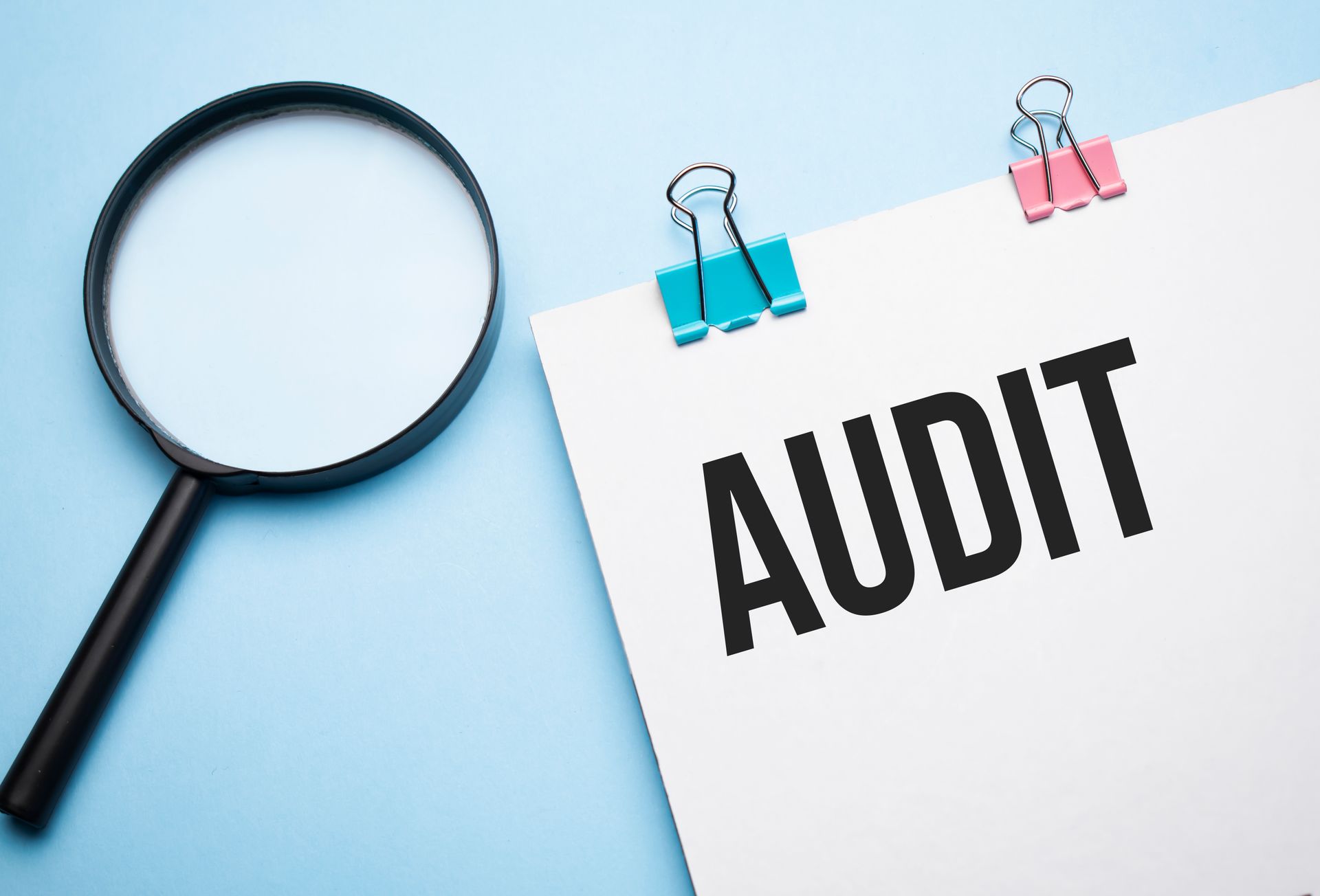 A magnifying glass is sitting next to a piece of paper that says audit.