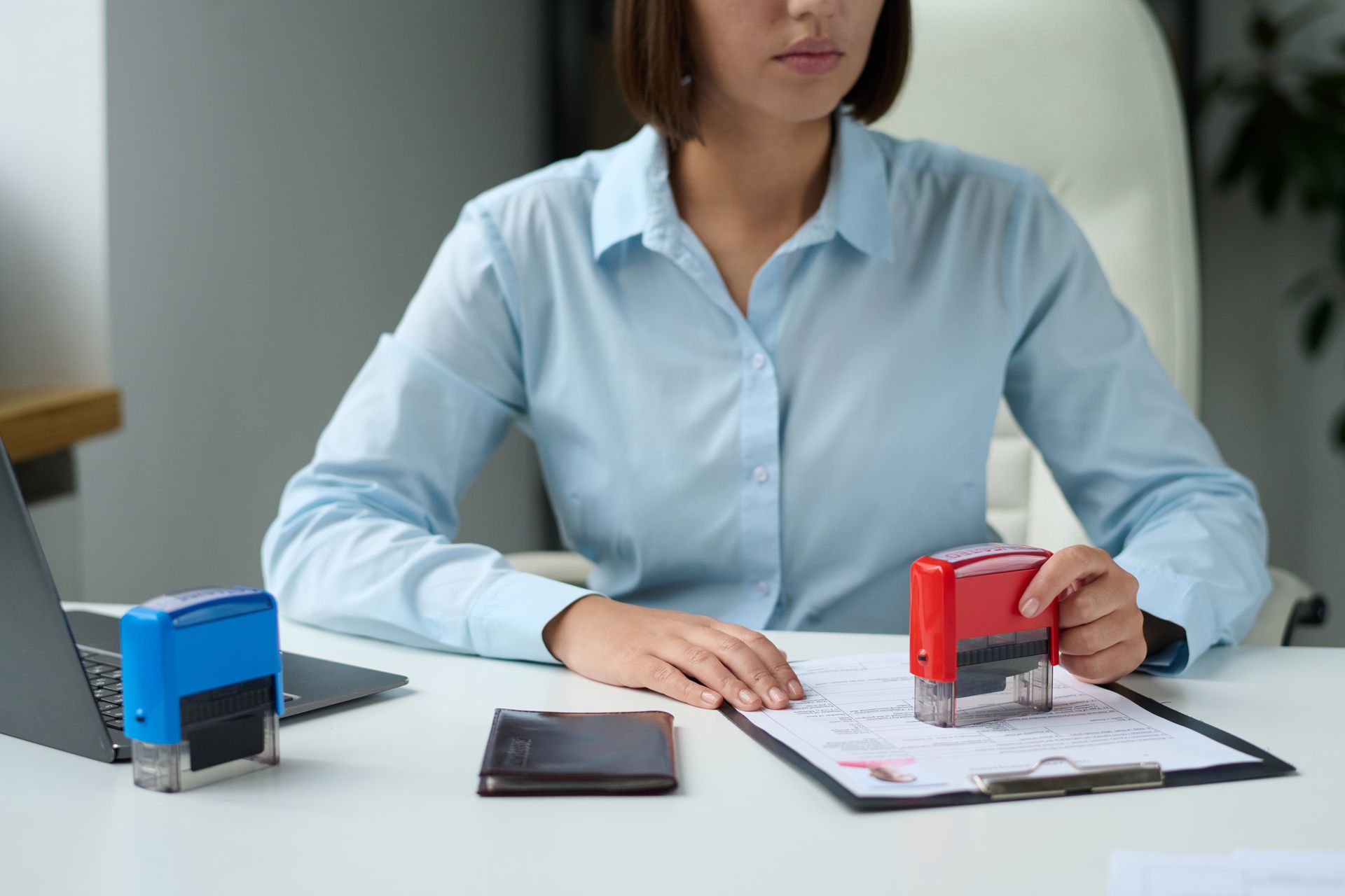 A woman is sitting at a desk using a stamp on a piece of paper.