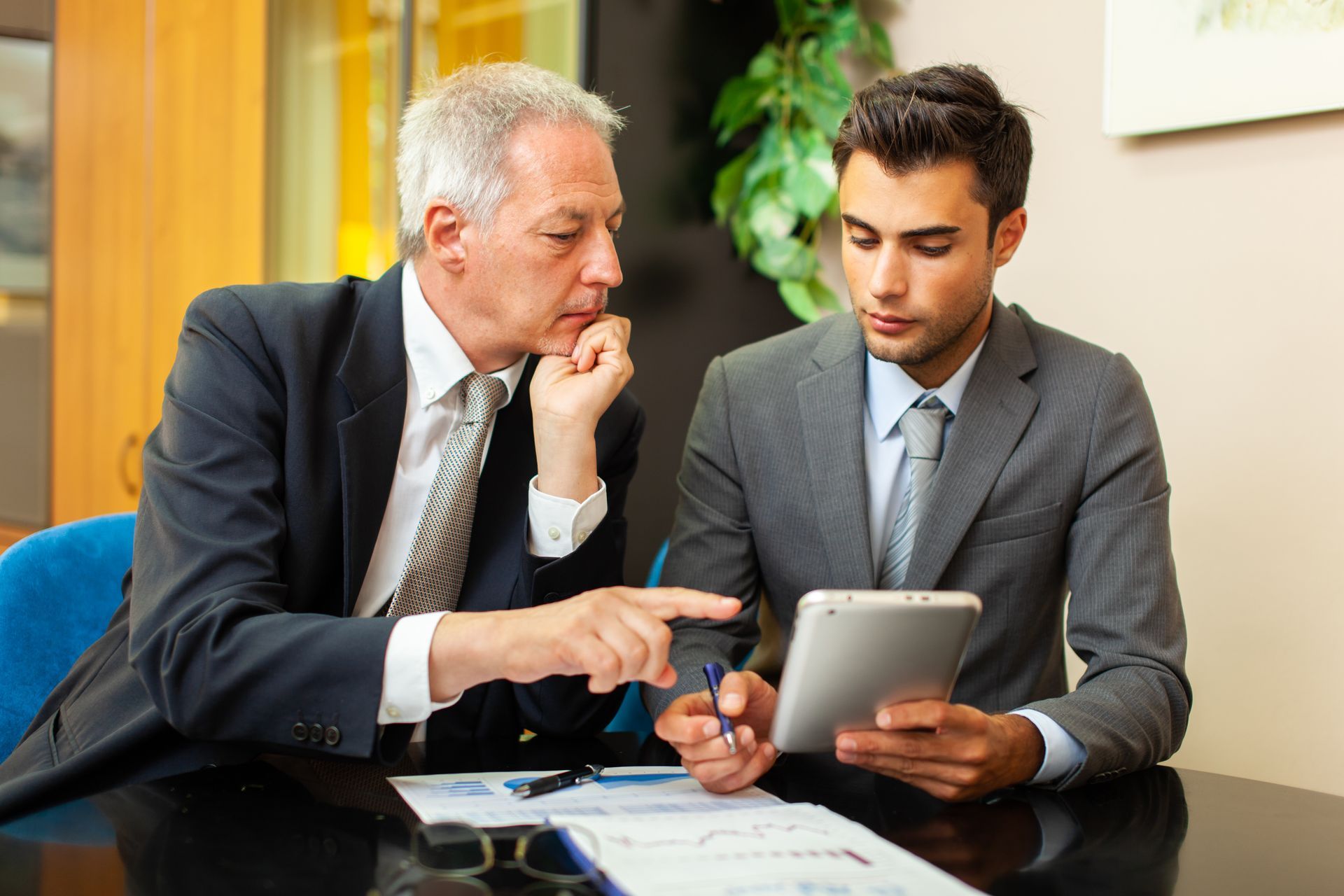 Two men are sitting at a table looking at a tablet.