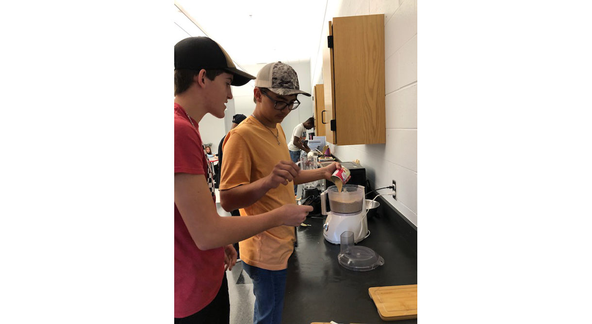 two young men are standing in a kitchen preparing food .