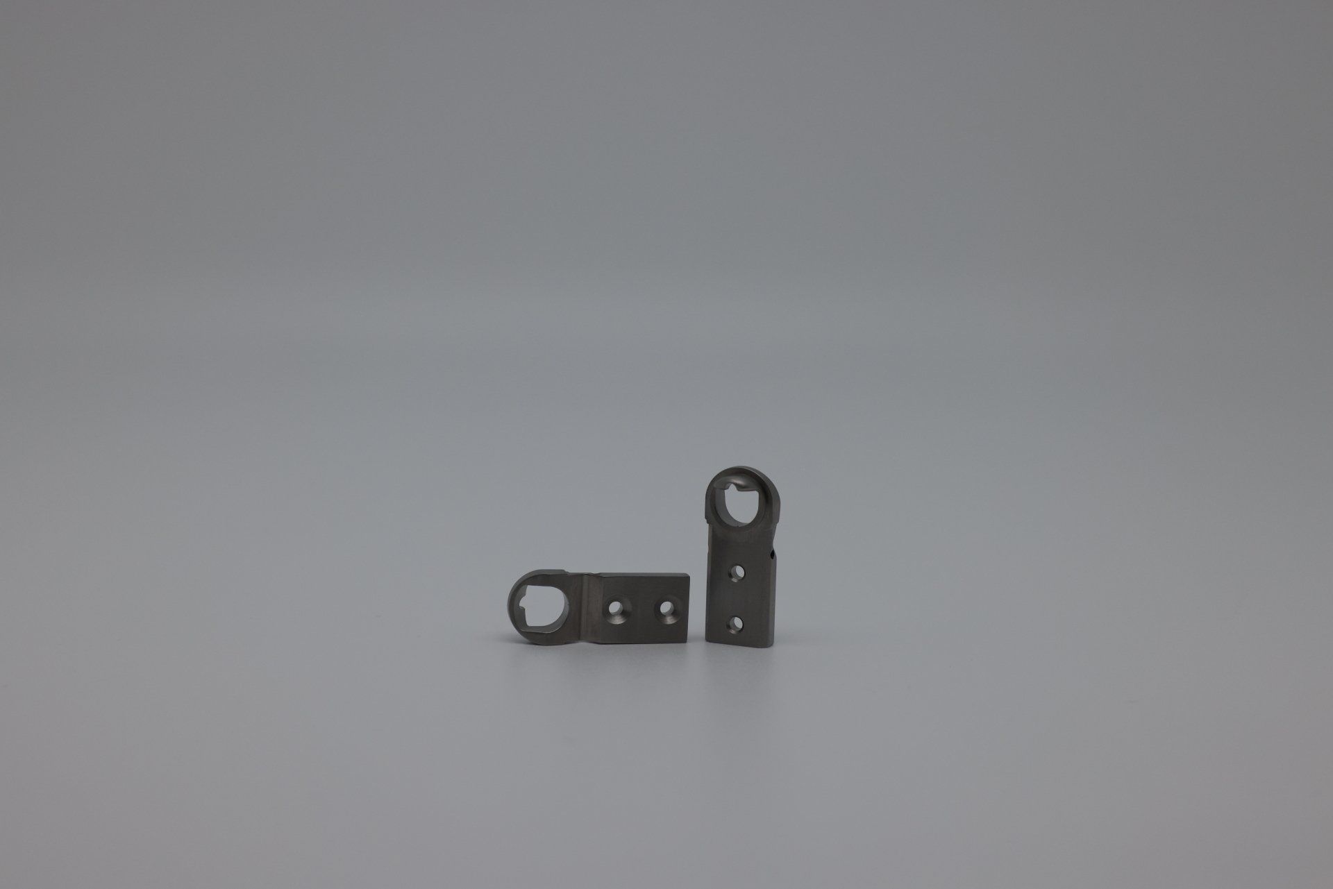 Two small metal pieces with holes in them are sitting on a gray surface.