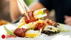 Chopsticks lifting a stuffed cabbage roll with rice and vegetables on a plate