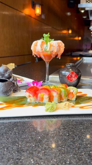 Sushi platter on a bar counter with colorful rolls and a martini glass of sashimi, in a dim restaurant.