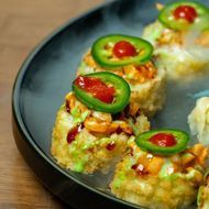 Sushi rolls topped with cucumber slices and red sauce on a dark plate