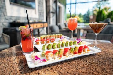 Sushi platter with colorful rolls and cocktails on a restaurant table by a window