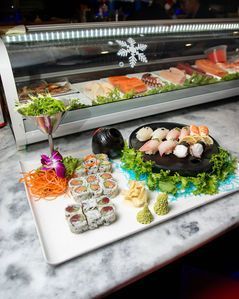 Assorted sushi rolls and nigiri on a white platter at a restaurant display counter
