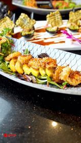 Assorted appetizers on platters, including skewered fried bites and stuffed rolls, garnished with sauce and greens